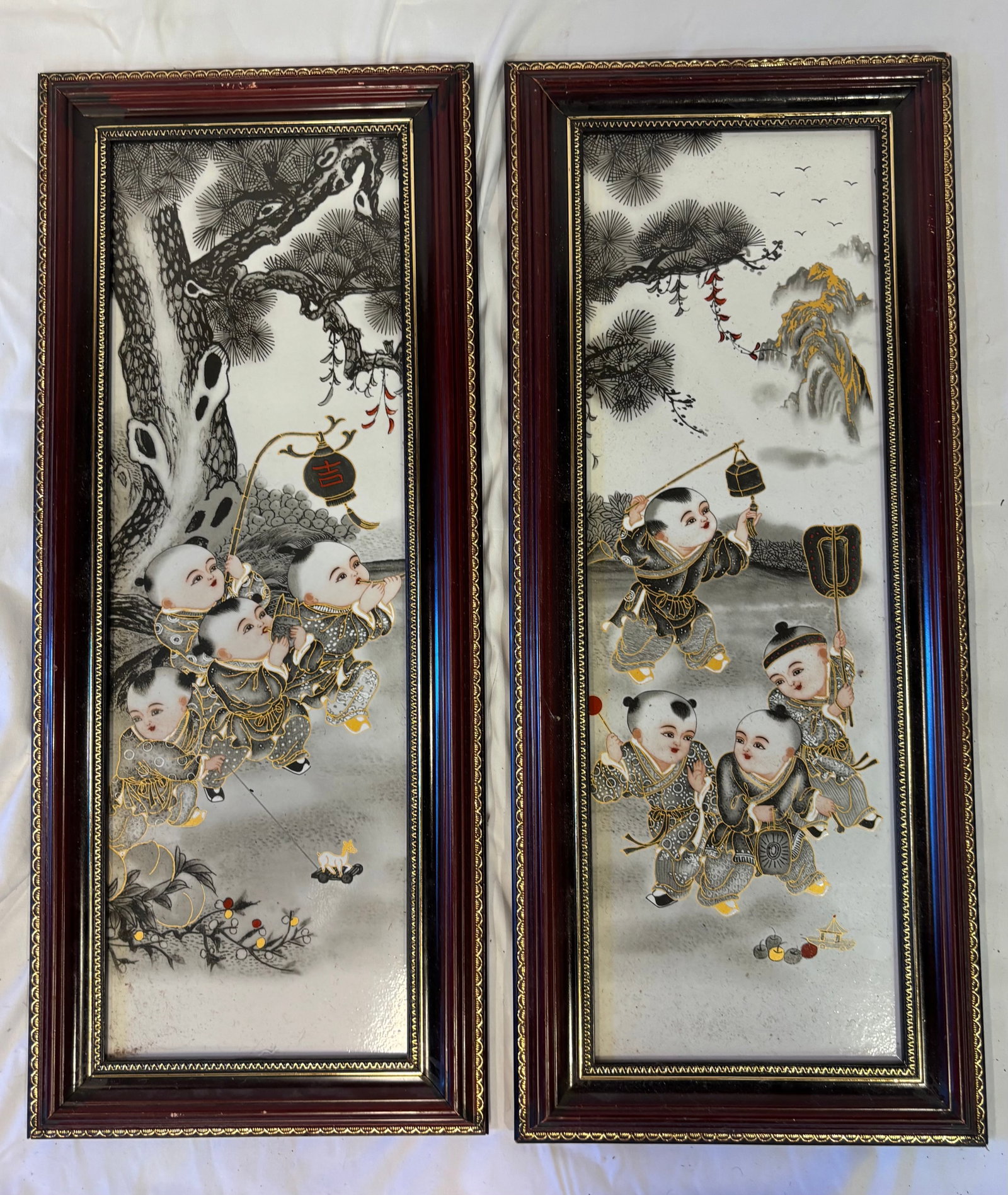 Pair of Chinese porcelain plaques: A pair of Chinese polychrome-painted porcelain plaques depicting lively groups of children at play in mountainous garden landscapes beneath pine trees. The festive scenes incorporate auspicious Chines