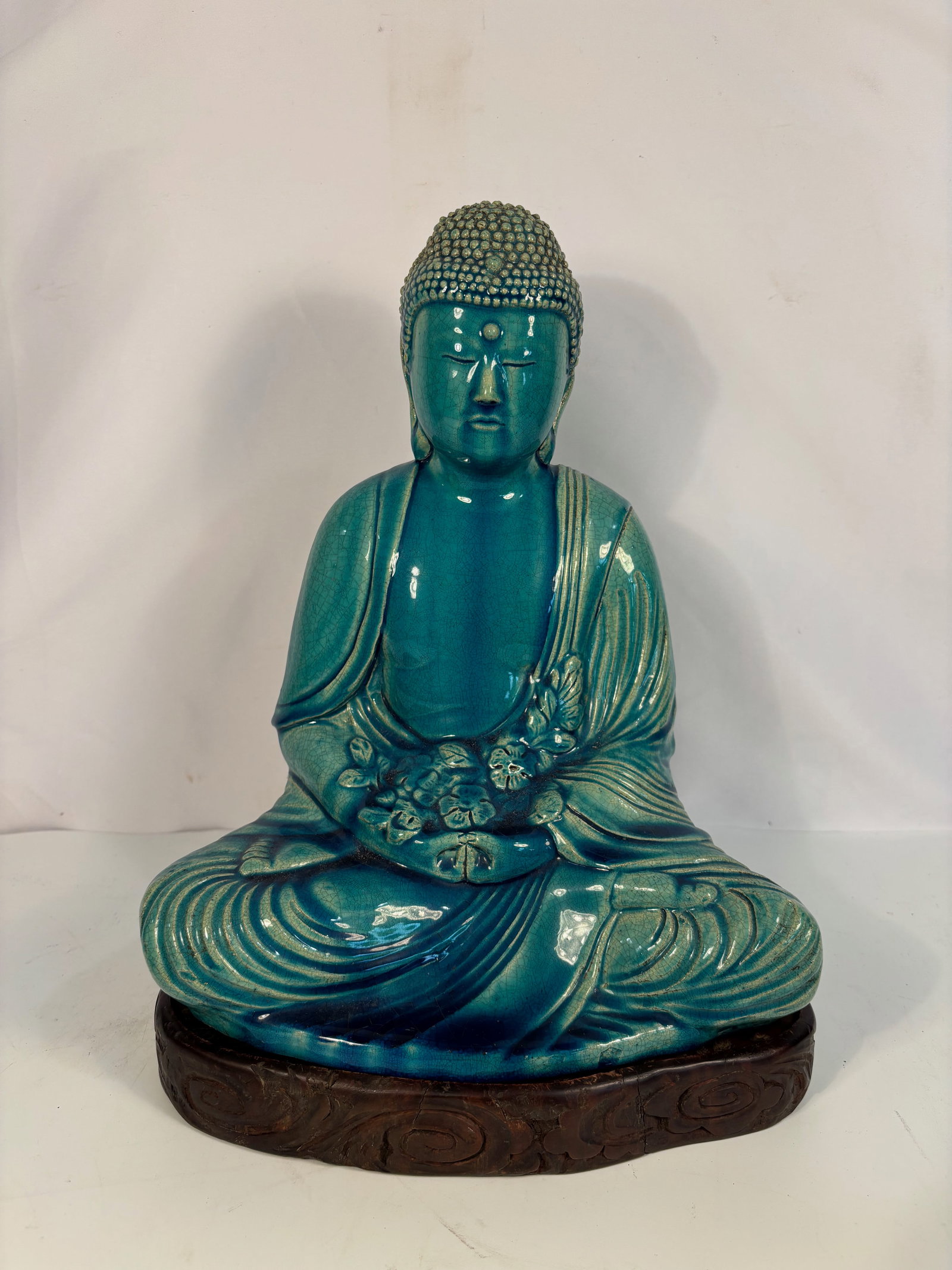 A Japanese Turquoise-Glazed Seated Buddha, Marked Meiji Nensei (1868–1912): A finely modeled Japanese porcelain figure of Buddha seated in meditation, covered in a luminous turquoise-blue crackle glaze pooling in the folds of the robe. The reverse impressed with a square