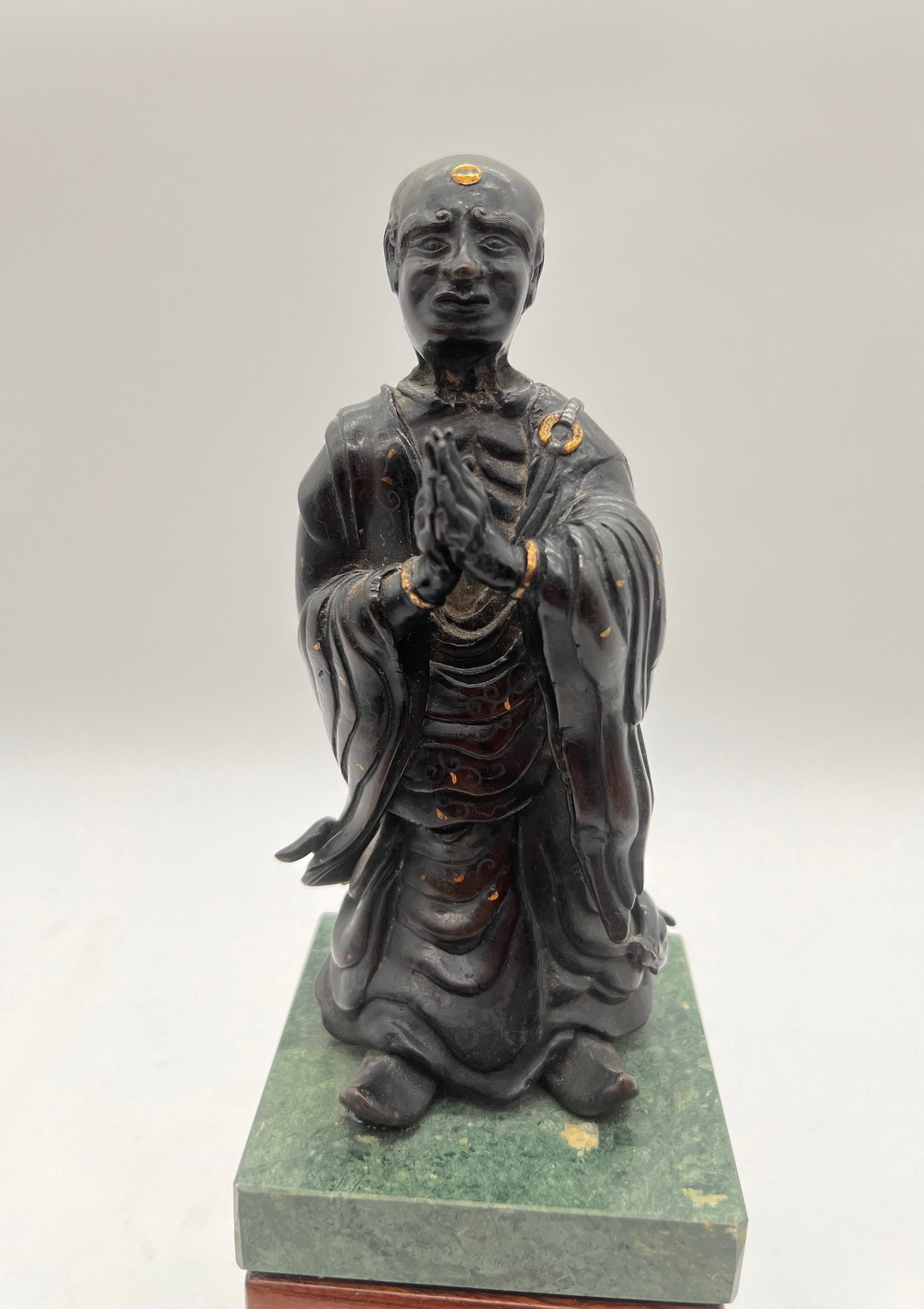 A Japanese silver inlaid gilt bronze monk statue with marble vase: 19th century ; The statue depicted in the images appears to be a bronze or brass figure of a Buddhist monk or an enlightened being (arhat or luohan). The statue has silver inlaid and gilt on the