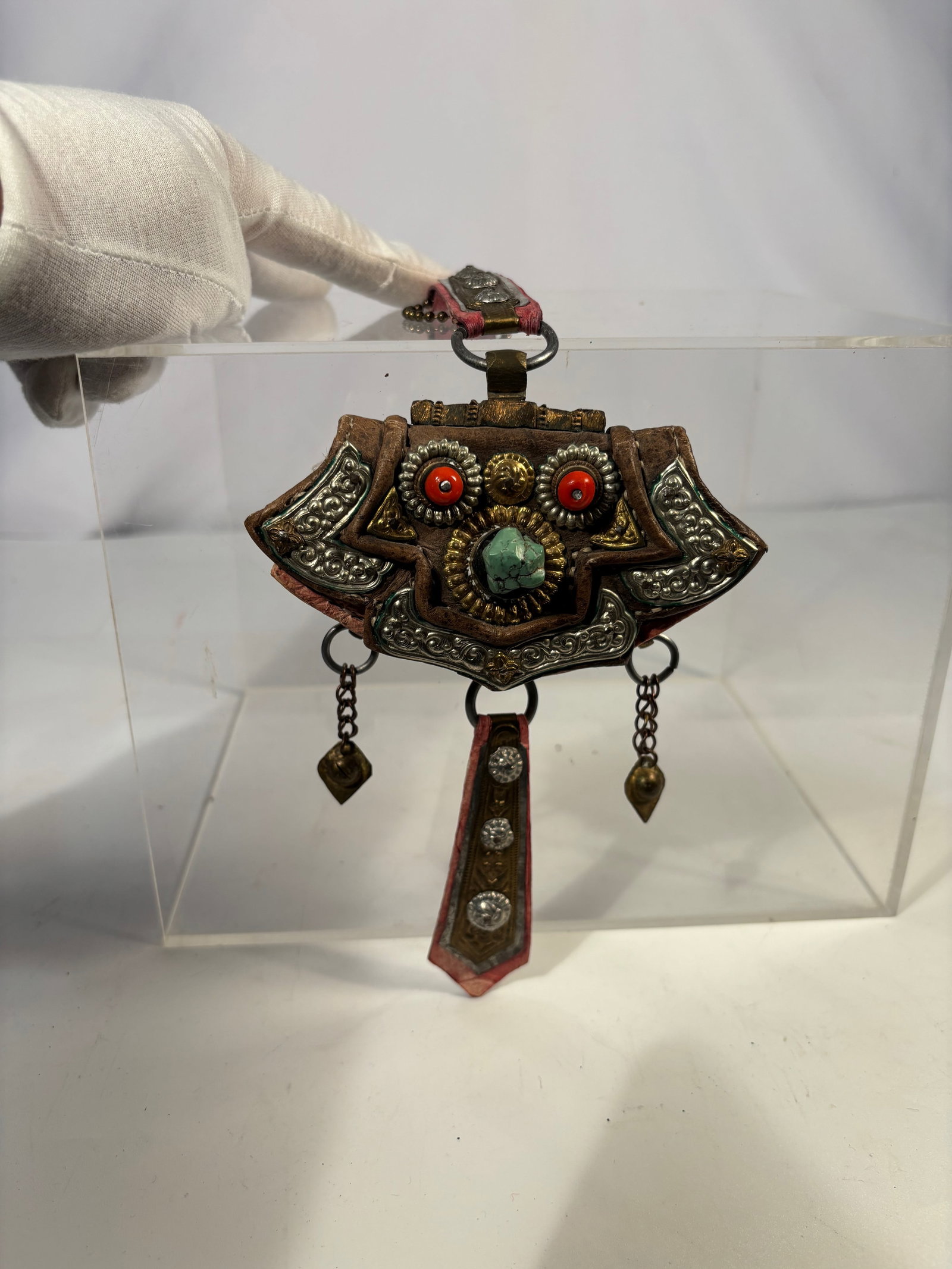A Tibetan Leather Gau Amulet with gilted Brass Studs and Pendant Drops, 19th century: Tibetan gau-style amulet, 19th to early 20th century, constructed of stitche d leather with applied brass studs and metal fittings. The amulet is of shield-like form and designed to be worn suspended,