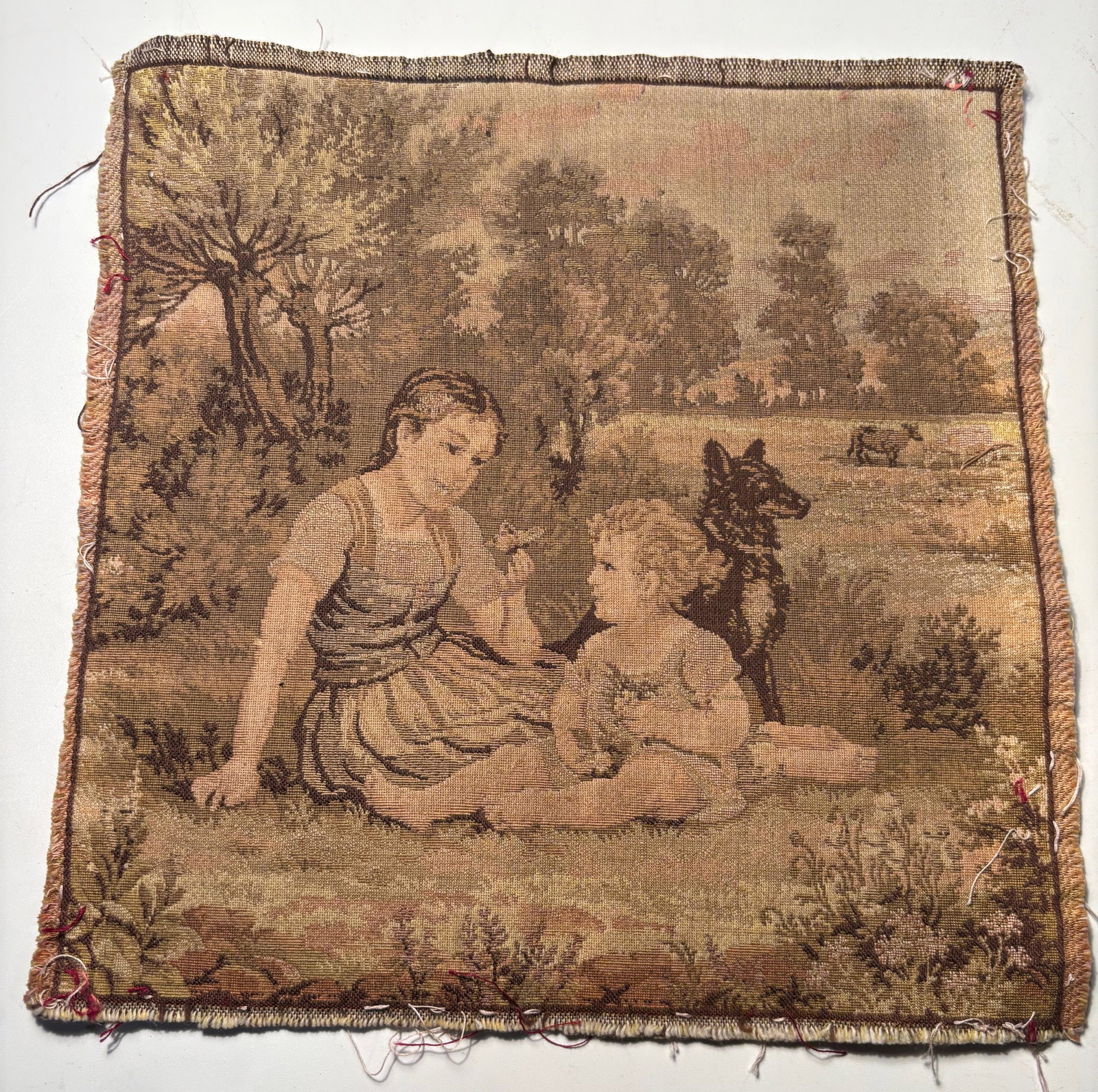 A Continental European Pastoral Tapestry Panel, Late 18th–Early 19th Century: Small Continental European woven tapestry panel, late 18th to early 19th century, depicting a pastoral scene with children and a dog in a wooded landscape. Rendered in muted earth tones with visible w