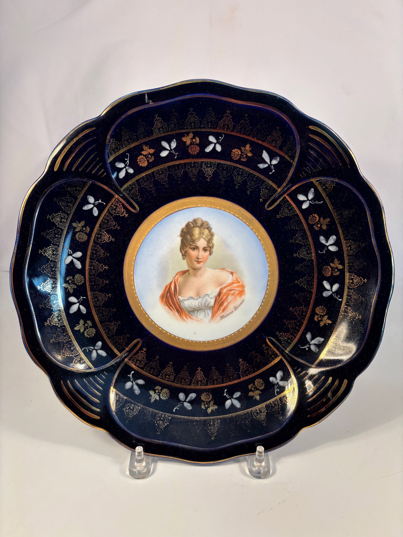 A German IPF Hand-Painted Porcelain Portrait Plate “Madame Récamier?? Circa 1900: A finely hand-painted porcelain portrait plate depicting Madame Récamier, signed lower right, on a cobalt-blue ground with gilt floral scrollwork and scalloped rim. Marked with gold “IPF Germany&rd