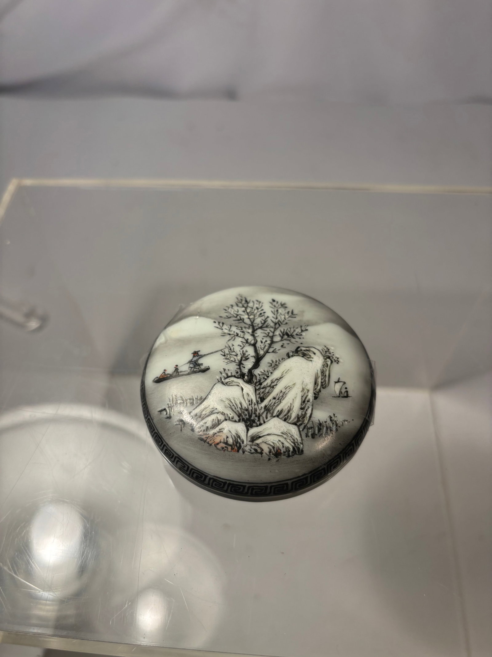 Chinese Grisaille Landscape Porcelain Ink Box, Qianlong Mark: A Chinese circular porcelain ink box with fitted lid, painted in grisaille and subtle iron-red enamels with a mountainous river landscape depicting trees, rockwork, figures in a boat, and distant arch