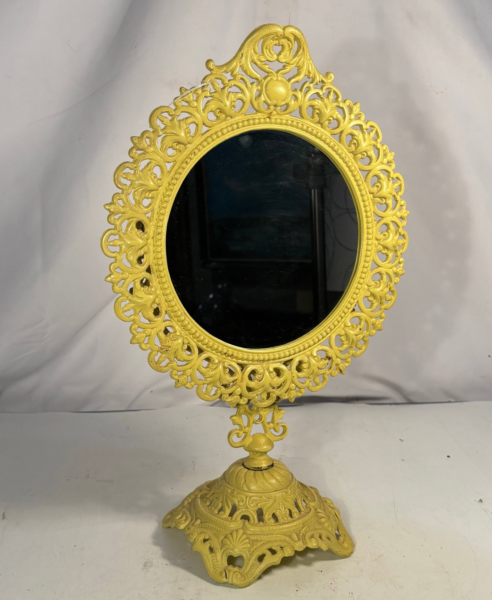 Antique 1890s–1930s Cast-Iron Standing Swivel Vanity Mirror: An antique late Victorian to early 20th-century tabletop vanity mirror featuring an oval swivel mirror within an ornate openwork cast-iron frame. Decorated with scrolling foliate motifs, a pierced cre