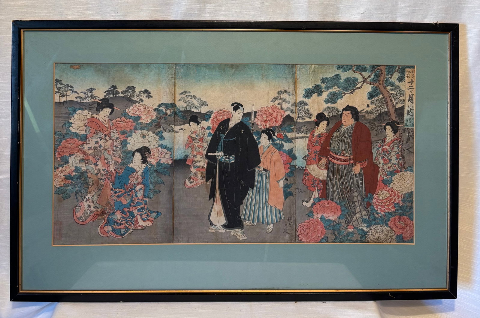 Utagawa Kunisada 1786–1864, Japanese Woodblock Print Triptych, Figures & Samurai Scene: A Japanese woodblock print triptych depicting figures in traditional attire, including a central samurai figure surrounded by attendants and women within a landscape setting featuring flowering plants