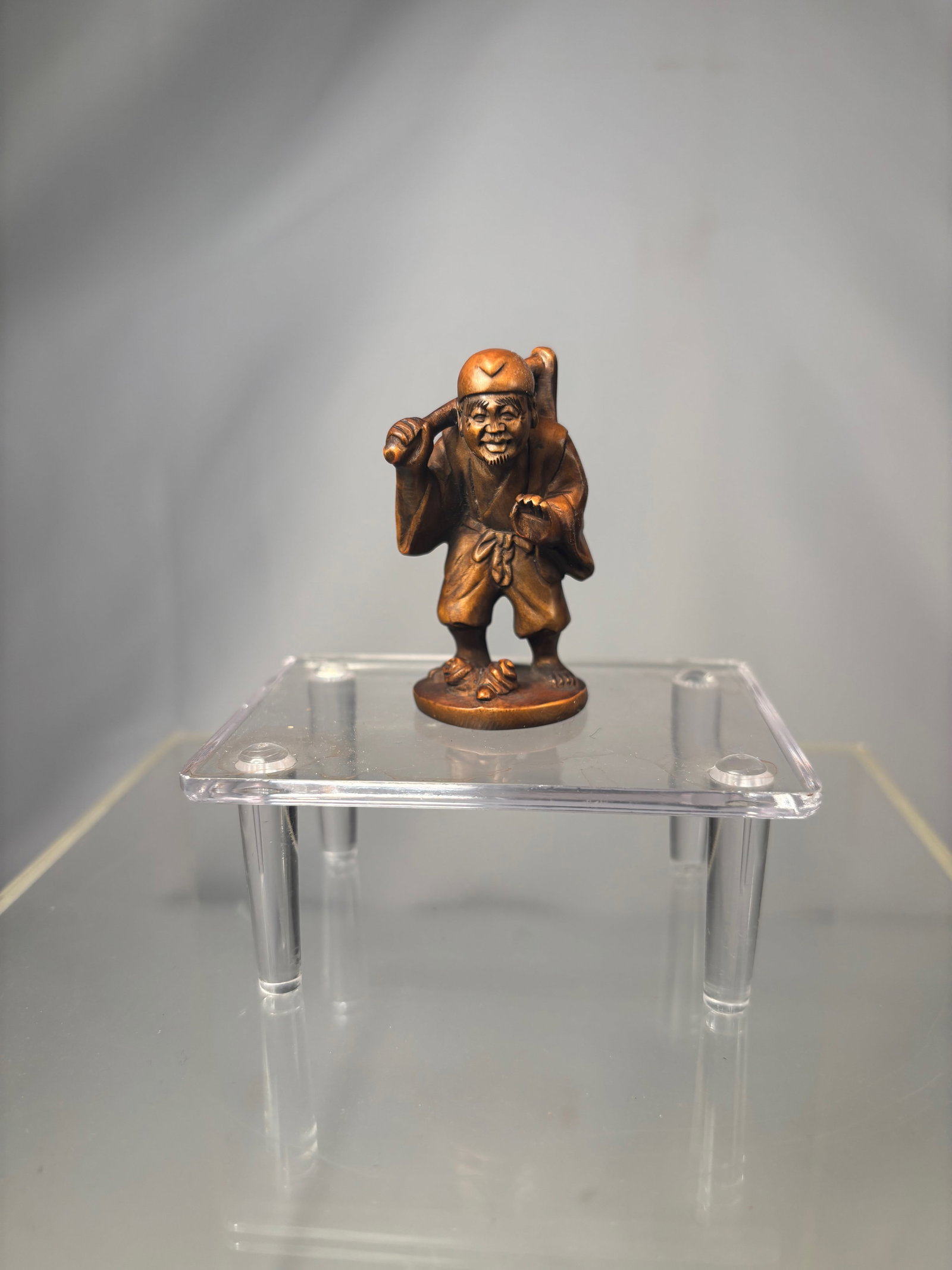A Japanese Boxwood Netsuke of a Standing Farmer Carrying a Hoe, Signed Gyokumatsu: Meiji period (19th century), Carved Japanese boxwood netsuke depicting a standing farmer carrying a hoe slung over his shoulder, captured mid-stride with a lively, expressive face. The figure wears sh