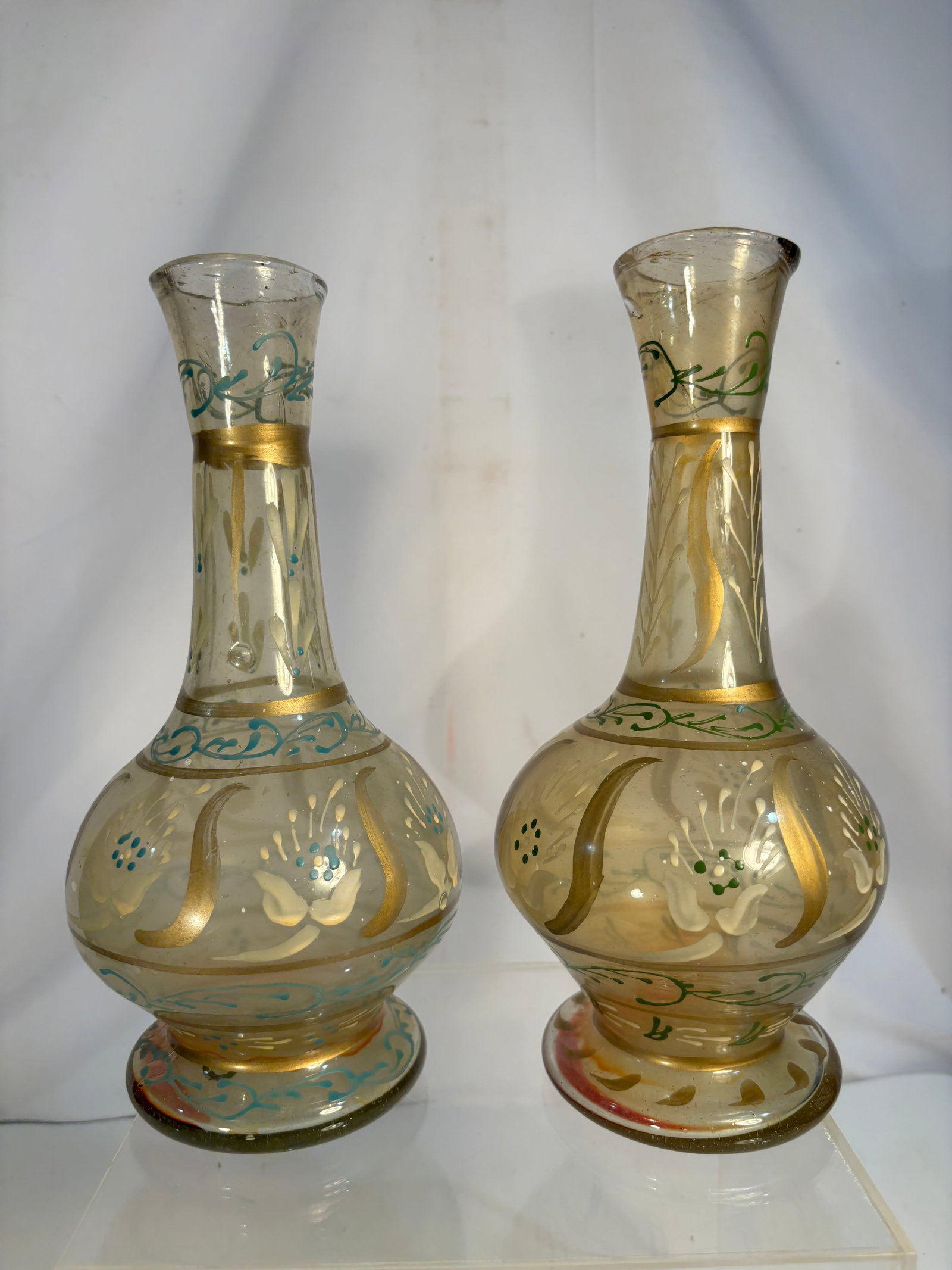 Pair of Antique Bohemian Enameled and Gilt Glass Vases: A pair of hand-blown amber-tinted glass vases, each of bulbous form with a tall slender neck and flared rim. Decorated throughout with hand-painted floral and scrolling motifs in turquoise, green, whi