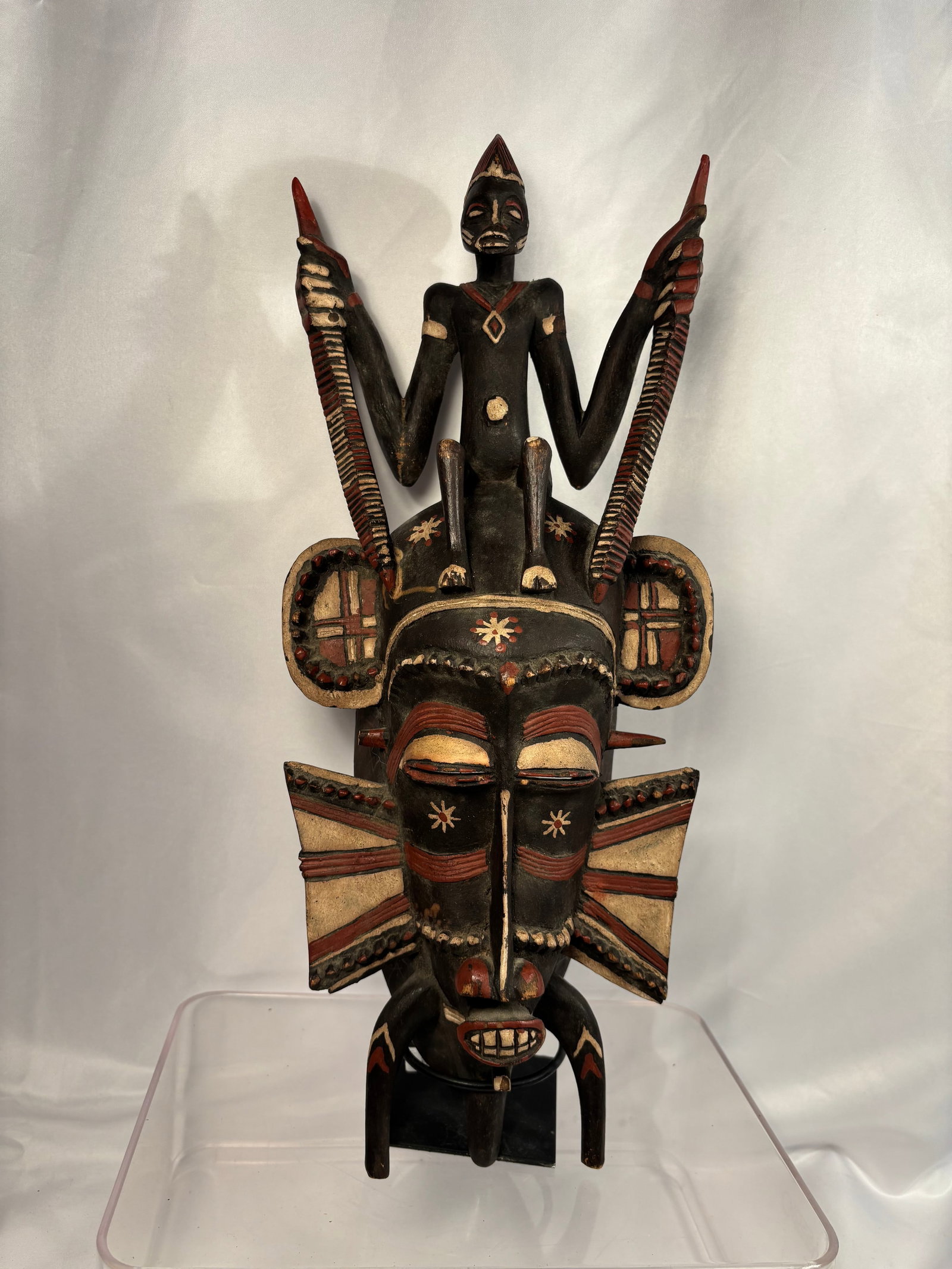 African Senufo Kpeliye Polychrome Carved Wood Mask with Seated Figure and Twin Hornbills: A polychrome carved wooden Kpeliye mask in the Senufo tradition of Côte d’Ivoire. The elongated anthropomorphic face features heavy-lidded eyes, a long central nose, a projecting mouth with carved 