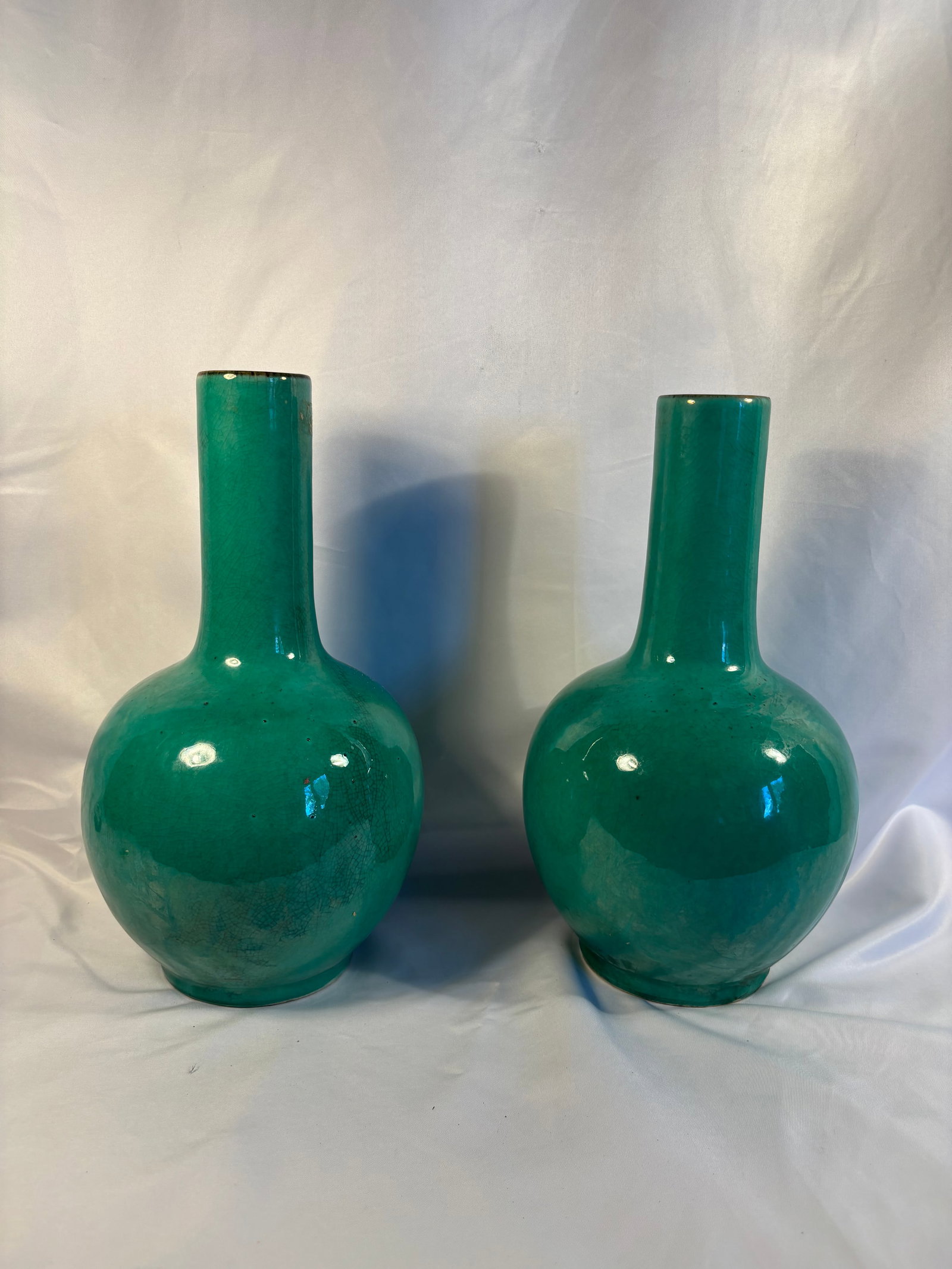 A Pair of Chinese Green Crackle-Glazed Porcelain Bottle Vases Qing Dynasty (1644-1912): A pair of Chinese porcelain bottle vases. Each is finely potted with a globular body rising to a tall cylindrical neck, the exterior covered in a rich emerald-green glaze suffused throughout with dark