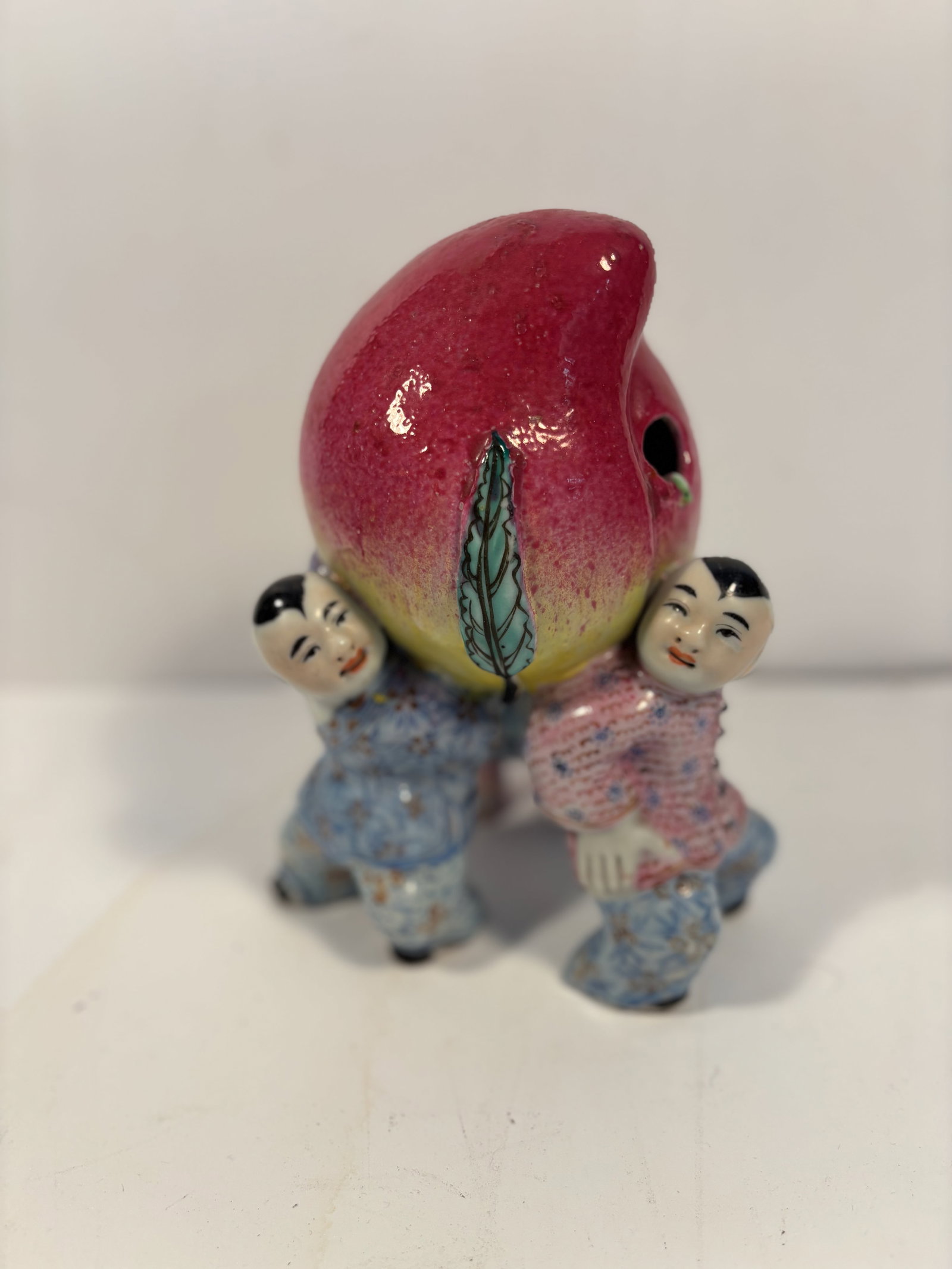 A Chinese famille rose Porcelain Figurine: 19th century; A beautifully crafted Famille Rose porcelain figurine depicting three boys joyfully holding a peach. Dimensions?HEIGHT: 8 inches; Width: 6 inches; Depth: 5 inches.