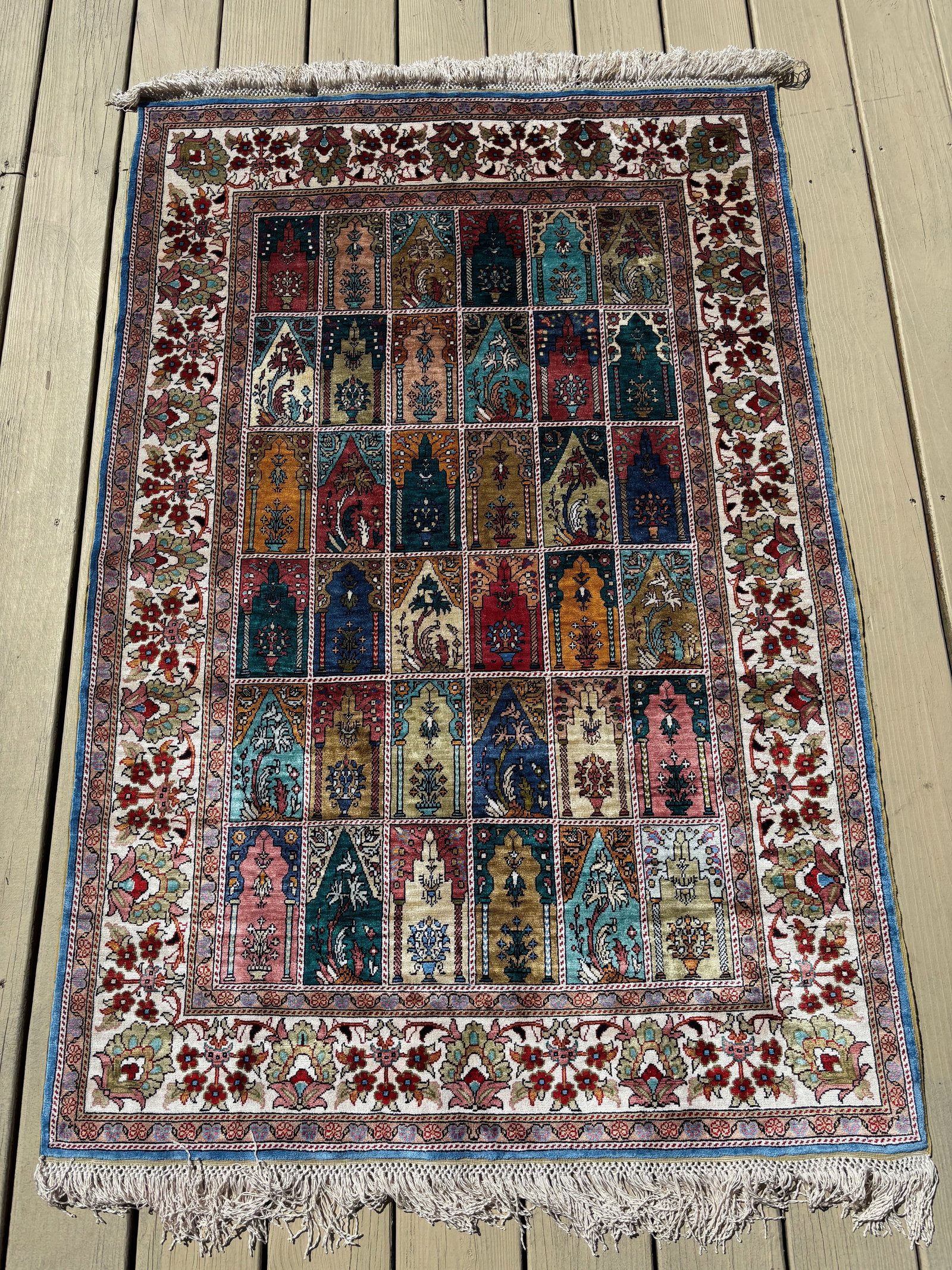 A Persian Silk Wall Hanging Rug with Prayer Niche Panel Design, Qum, 20th Century: A finely woven Persian silk rug from Qum, designed for use as a decorative wall hanging. The field is arranged in a garden of pointed prayer niches, each enclosing stylized floral vases in vivid jewel