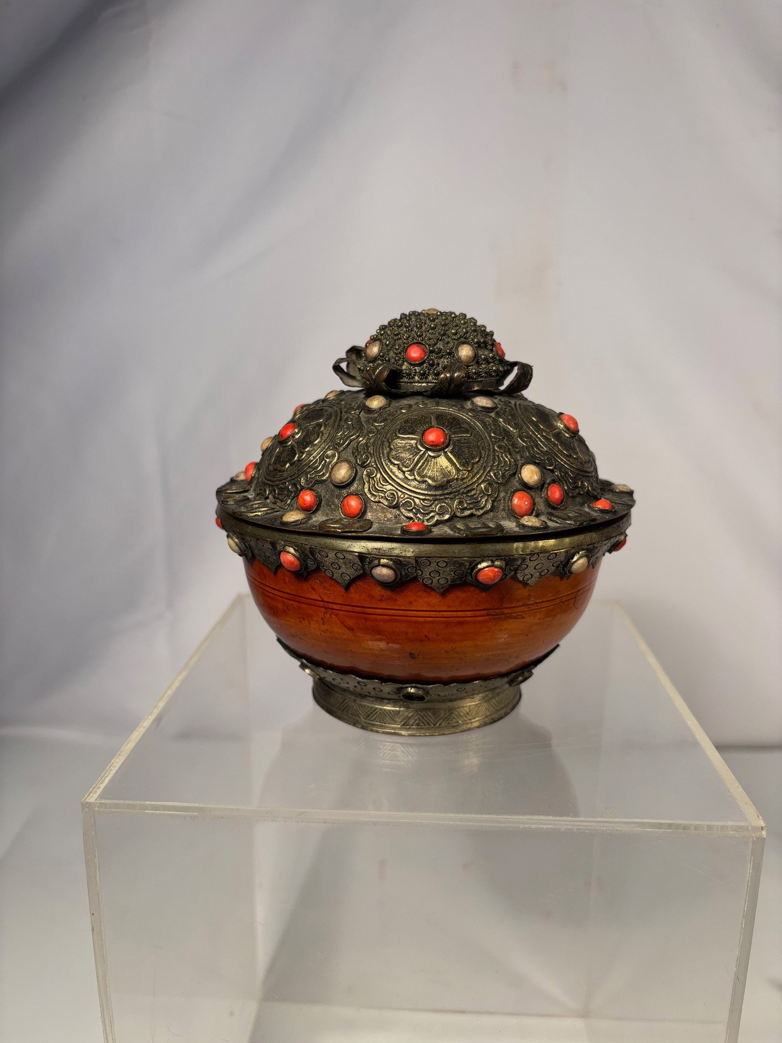 A Tibetan Metal-Mounted Covered Lacquer Bowl with Coral Inset Decoration, 19th Century: Tibetan or Himalayan metal-mounted covered bowl of rounded form with domed lid, richly decorated with repoussé and cast metalwork featuring scrolling and foliate motifs.extensively embellished with