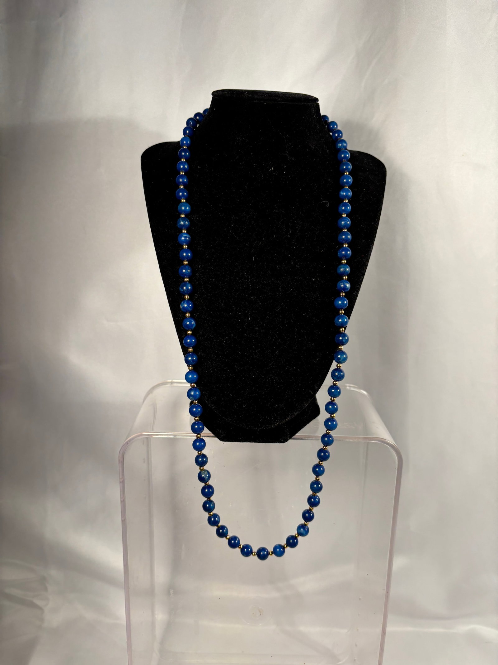 Long Lapis Lazuli Beaded Necklace with Gold-Tone Spacers: A long single-strand necklace composed of polished, irregular oval-form deep cobalt-blue beads, likely lapis lazuli, individually separated by small gold-tone spacer beads. The stones display natural-