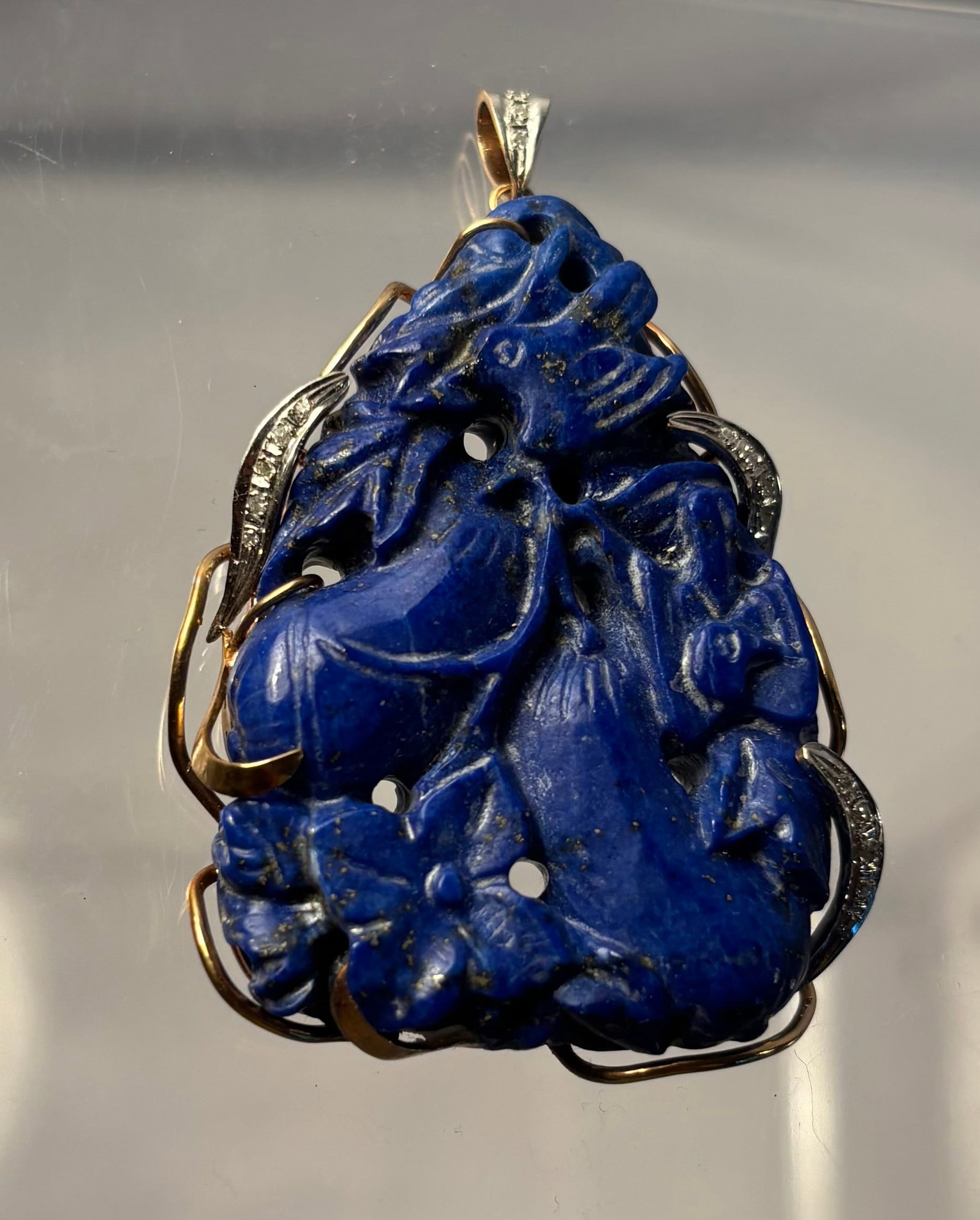 Carved Lapis Lazuli Bird and Fruit Pendant in 14K Gold with Diamonds: A large carved and pierced lapis lazuli pendant depicting birds amid fruit, blossoms, and leafy branches. The richly colored cobalt-blue stone displays scattered natural-looking pyrite inclusions and 