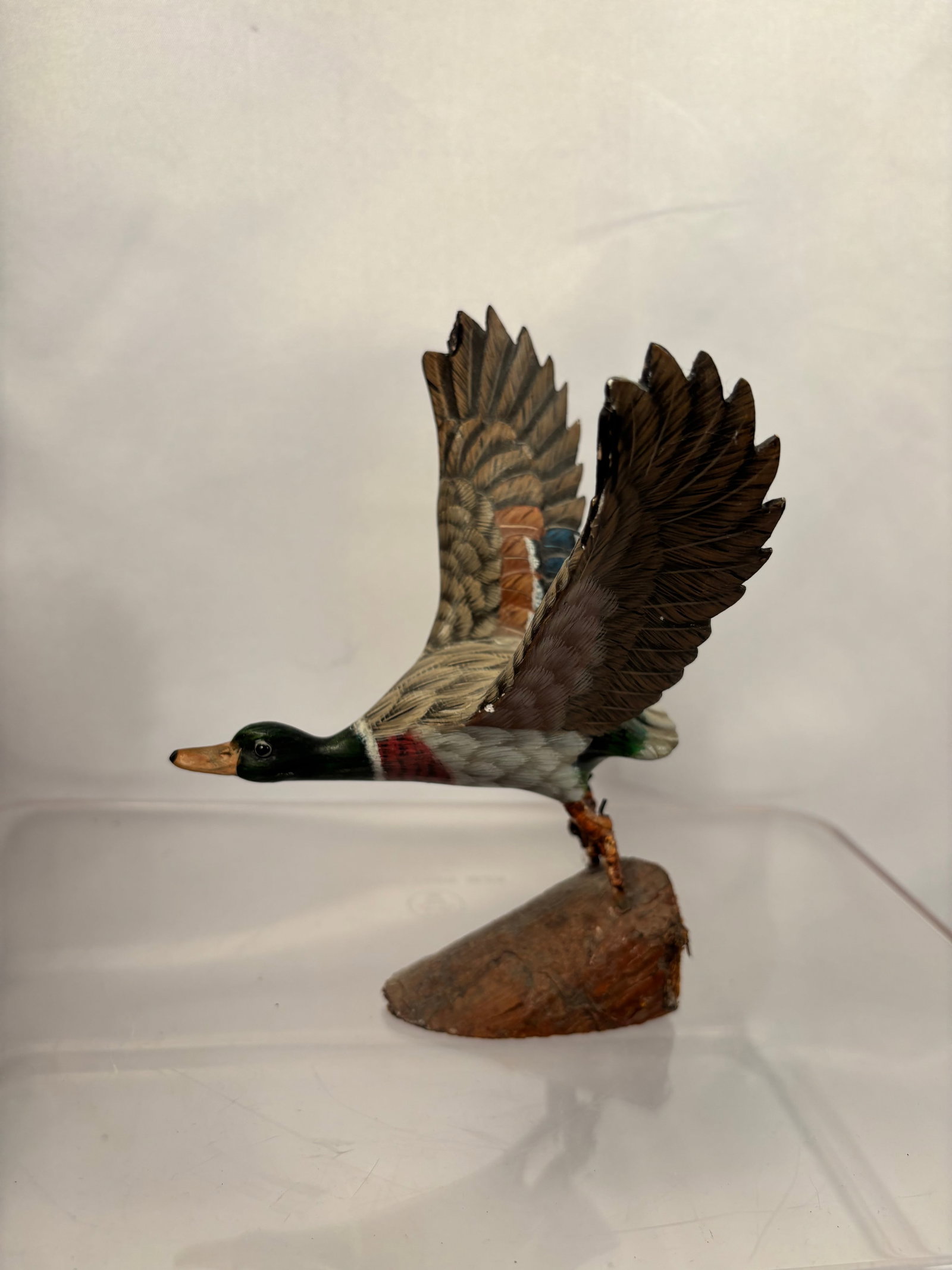 Hand-Carved and Painted Flying Mallard Drake Wood Sculpture on Base: A hand-carved and painted wooden sculpture depicting a mallard drake in flight, with its wings fully extended and legs lowered in a landing pose. The bird features a dark green head, chestnut breast, 