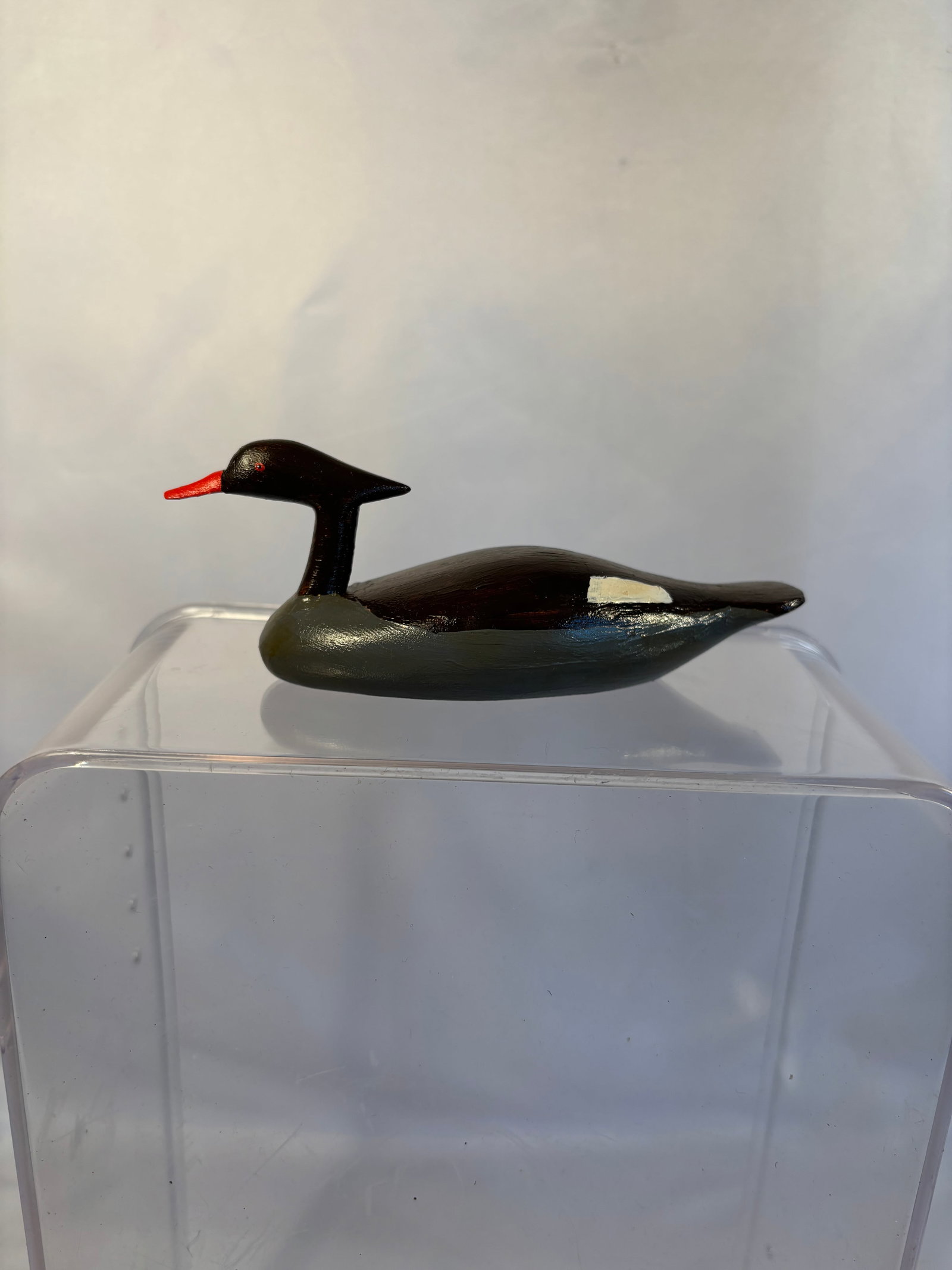 Hand-Carved and Painted Merganser Duck Decoy: A vintage hand-carved wooden waterfowl decoy, likely depicting a merganser, featuring a streamlined dark green and black body, elongated neck and head, bright red bill and eyes, and contrasting cream-