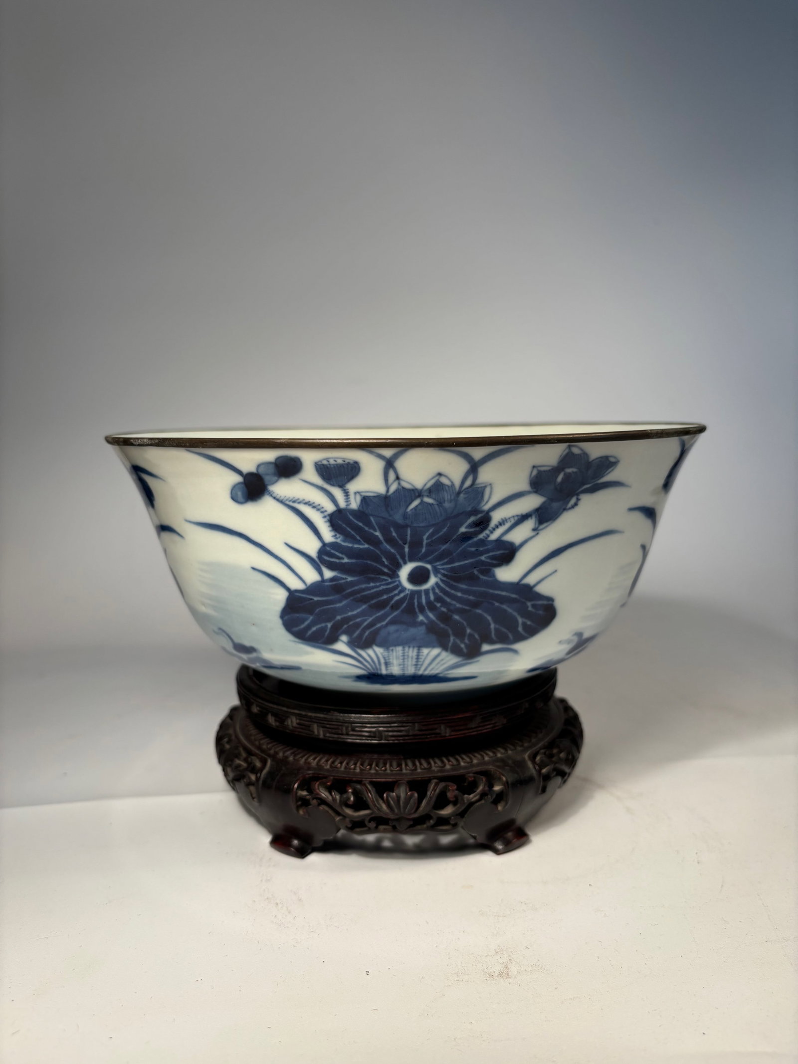 A Chinese Blue and White Porcelain Bowl with"zheng ruo shen cang" mark: kangxi period(1661-1722); Mounted with a Bronze Rim; A finely painted Chinese porcelain bowl featuring underglaze cobalt blue lotus blossoms and scrolling tendrils against a white ground. The floral d