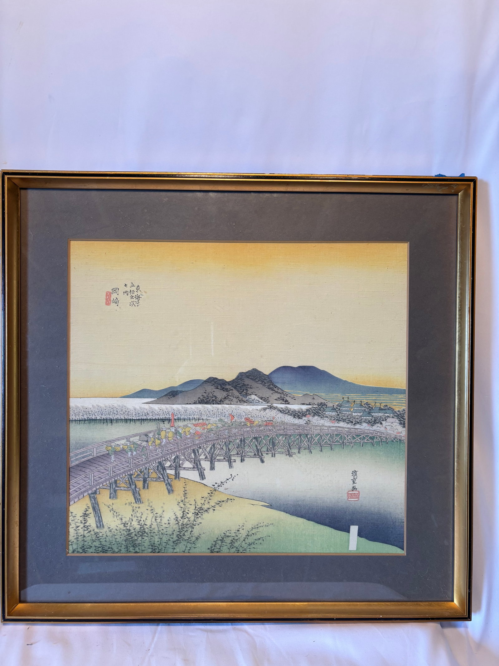 Japanese Utagawa Hiroshige “Okazaki?? from the Fifty-Three Stations of the Tokaido: Japanese color woodblock print depicting “Okazaki”, one of the celebrated scenes from the Fifty-Three Stations of the Tokaido series. The composition features a long wooden bridge crossing a r