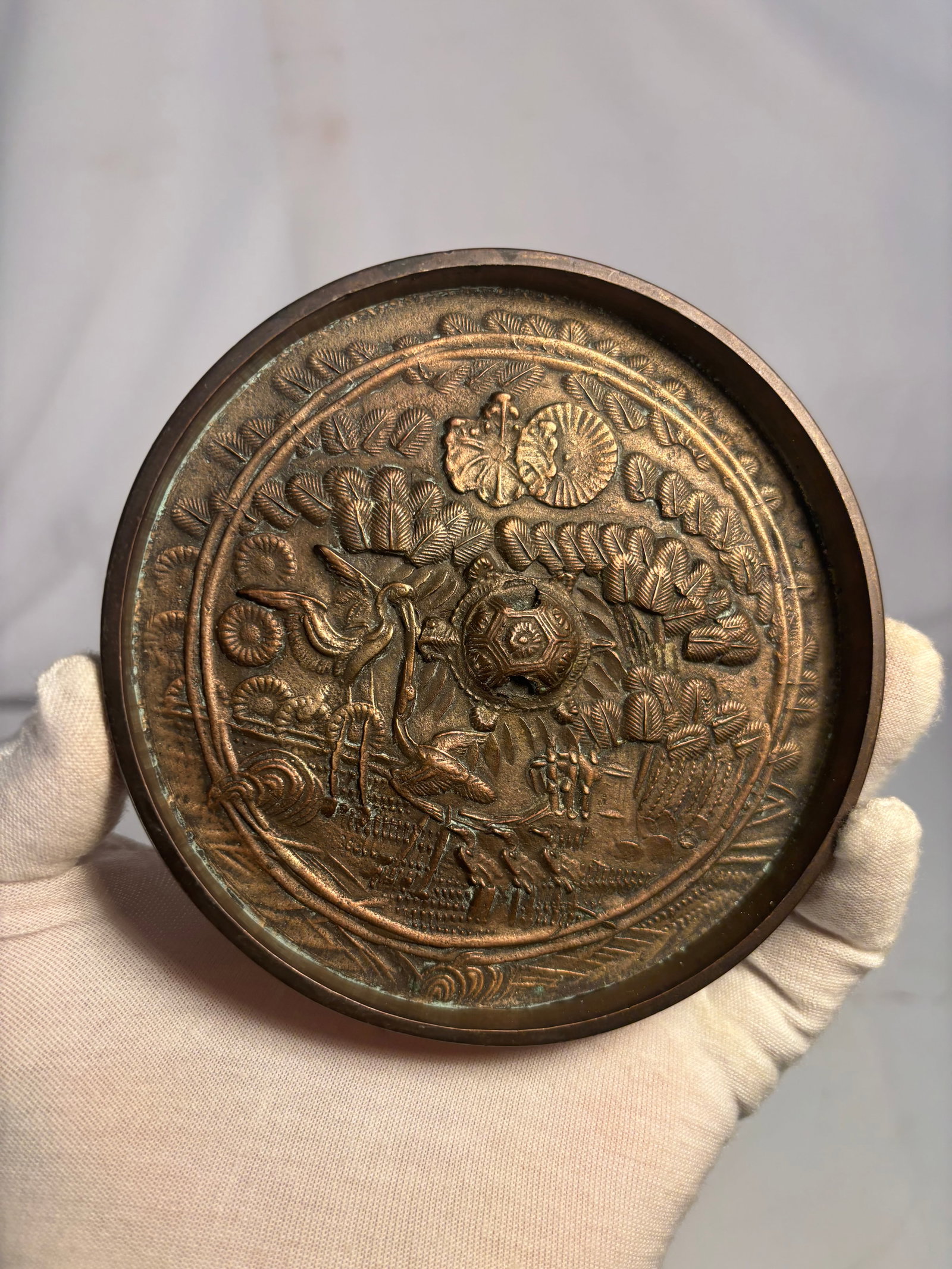 Antique Japanese Bronze Mirror with Crane and Tortoise, Tsuru-Kame Motif, Edo period (17th to 19th: An antique Japanese circular bronze mirror cast in relief with an auspicious landscape depicting cranes, a minogame long-tailed tortoise, pine, bamboo, and stylized waves. A pierced central knob allow