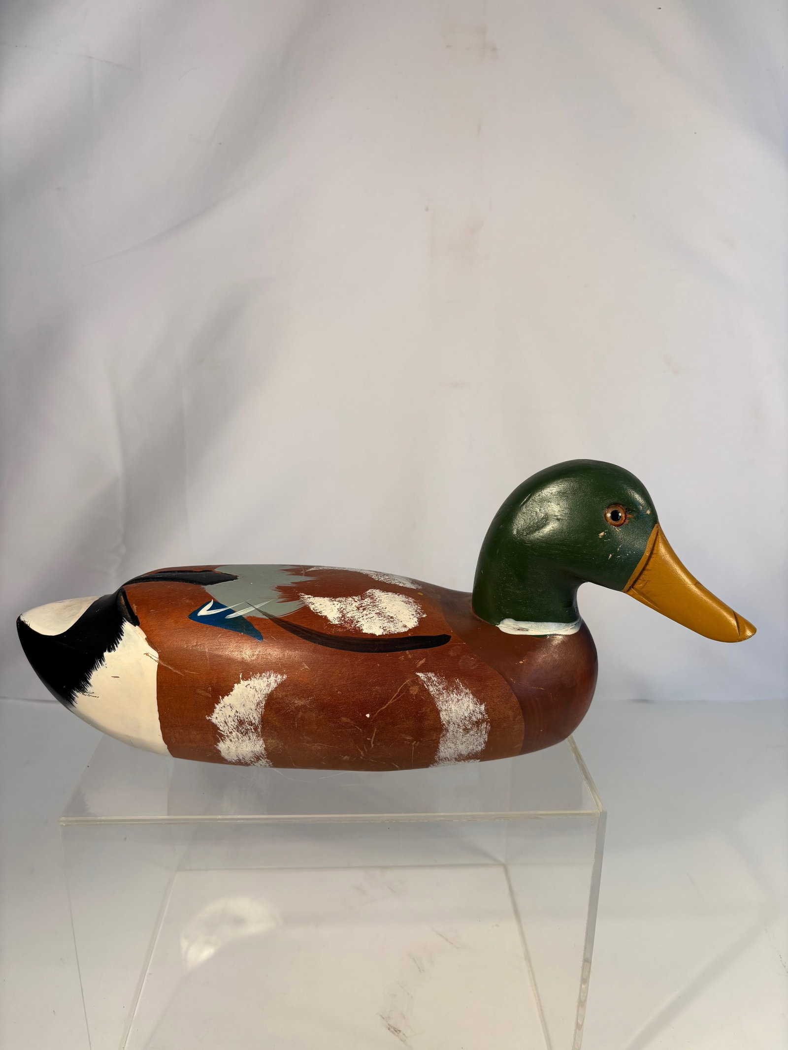 Hand-Carved and Painted Wooden Mallard Drake Decoy: A vintage hand-carved and painted wooden duck decoy depicting a mallard drake, with green head, yellow bill, and brown body with white and blue wing markings. Glass eyes, flat base, and original polyc