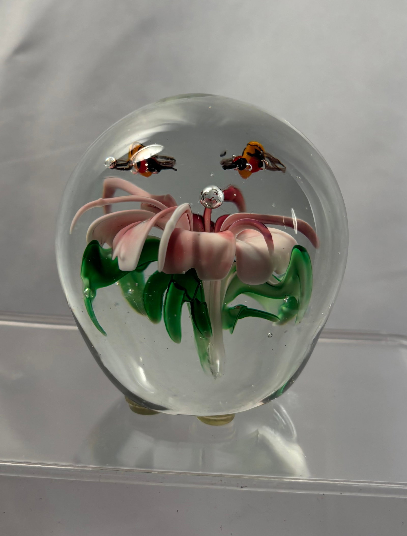 A Lampwork Art Glass Paperweight with Bees and Pink Flowers: A clear art glass paperweight containing a finely modeled lampwork arrangement of pink trumpet-form flowers and green leaves, with two hovering bees rendered in amber, black, white, and translucent gl