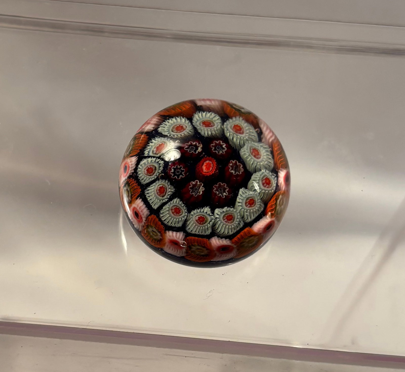 A Murano-Style Concentric Millefiori Glass Paperweight: A domed art glass paperweight containing a central red millefiori cane surrounded by three concentric rings of complex floral and cogwheel canes in white, red, pink, amber, and olive tones, arranged a