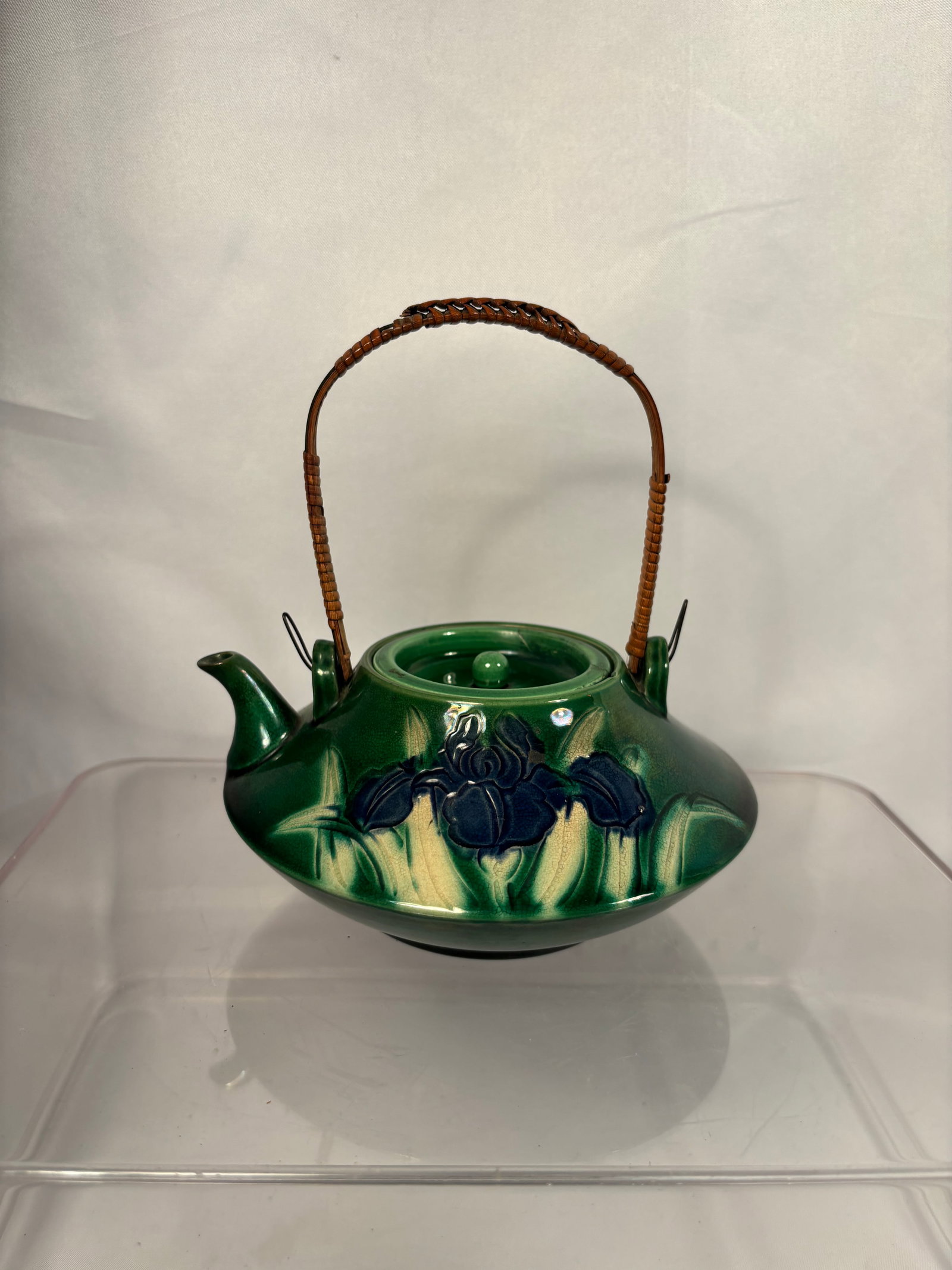 A Japanese Green-Glazed Ceramic Teapot with Iris Decoration: A vintage Japanese ceramic teapot featuring a distinctive flattened, low-profile body covered in a glossy deep-green glaze. The exterior is decorated with raised iris blossoms in dark blue and pale-ye