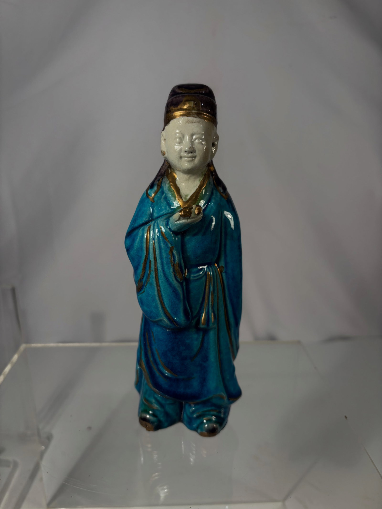 A Chinese Blue-Glazed Porcelain Figure with Gold Highlights: Qing dynasty(1644-1912) ; A Chinese glazed porcelain figure, decorated in rich turquoise and deep blue glazes with gilt accents. The standing figure is shown holding a small object in one hand and