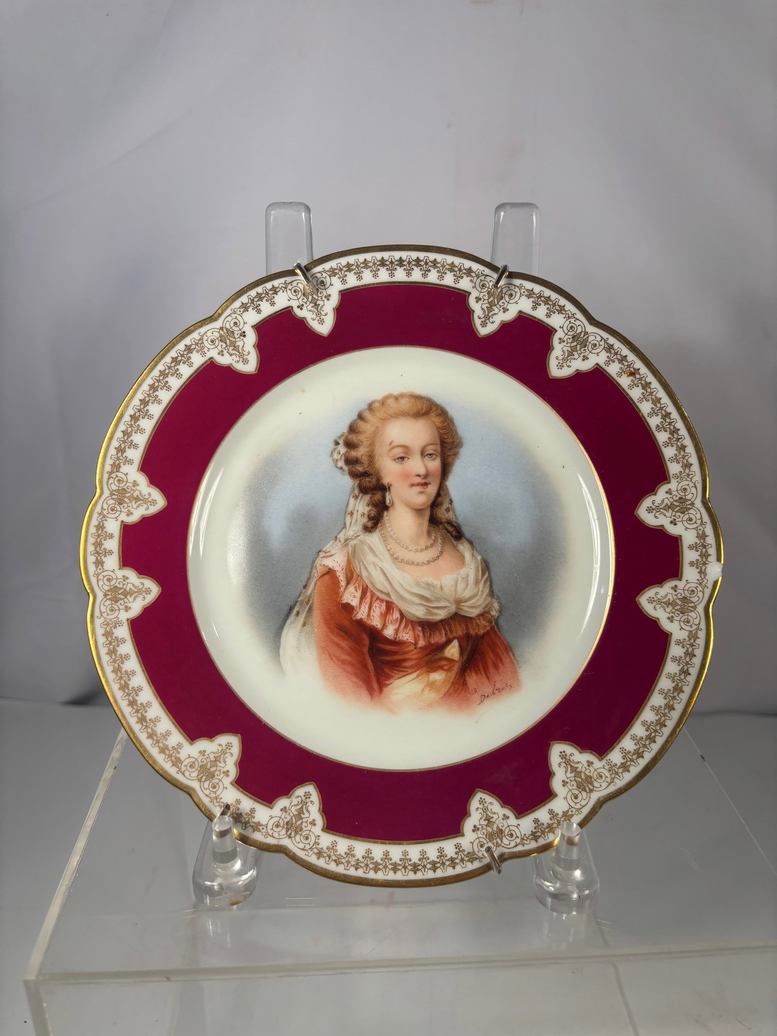 A European Hand-Painted Porcelain Portrait Plate of Marie Antoinette: European porcelain decorative plate featuring a finely hand-painted portrait of Marie Antoinette at center, surrounded by a deep ruby-red border with gilt ornamental detailing. The reverse bears paint