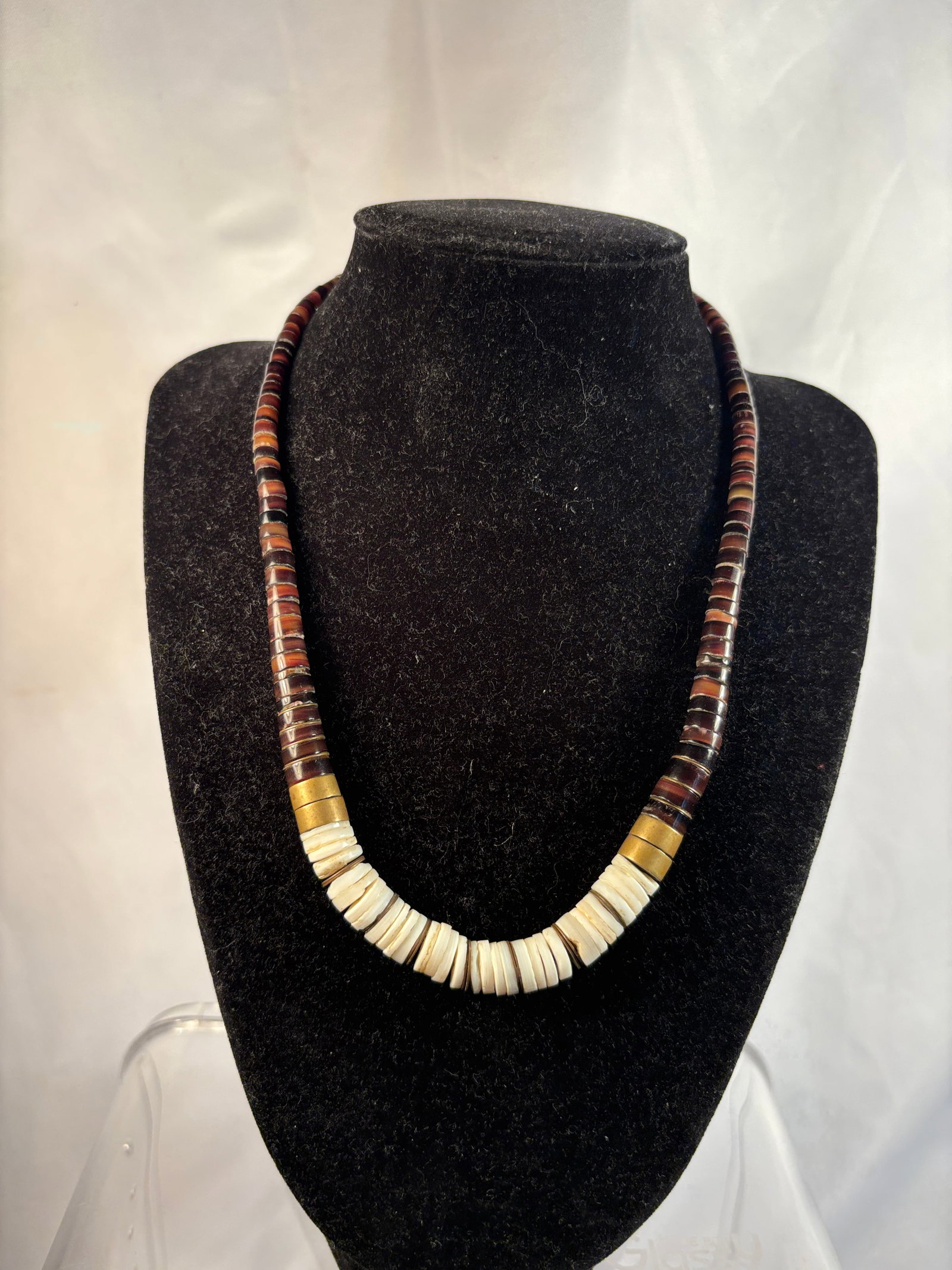 Vintage Shell and Brown Heishi Bead Necklace: A vintage heishi bead necklace featuring numerous finely cut dark brown disc beads accented by a central arrangement of creamy white shell heishi beads. Decorated with metal spacer rings and brass-ton