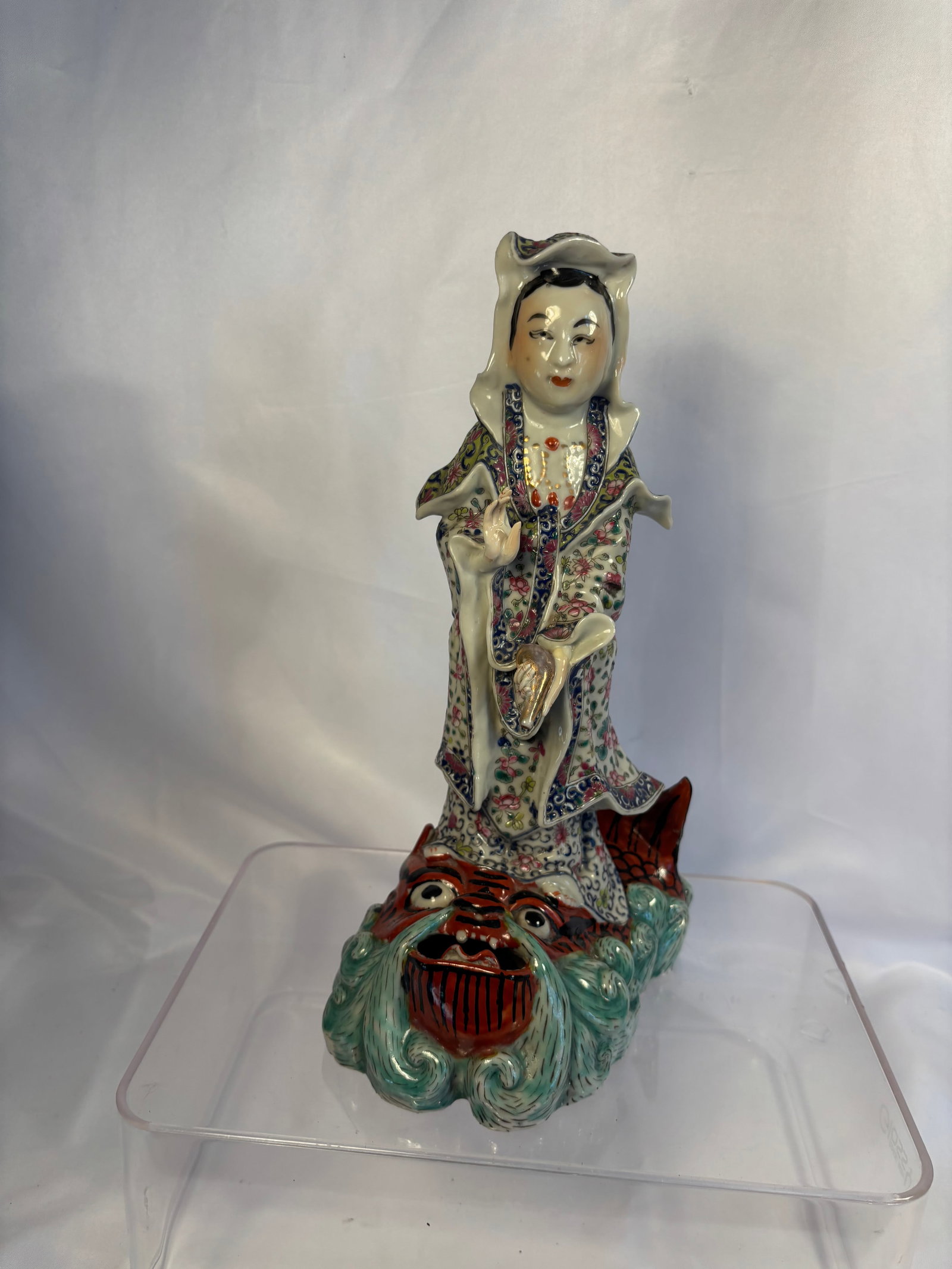 A Chinese Famille Rose Porcelain Figure of Guanyin on Dragon: A Chinese famille rose porcelain figure of Guanyin, finely modeled standing upon a dramatic dragon and wave-form base. The deity is depicted wearing elaborate flowing robes densely decorated with colo