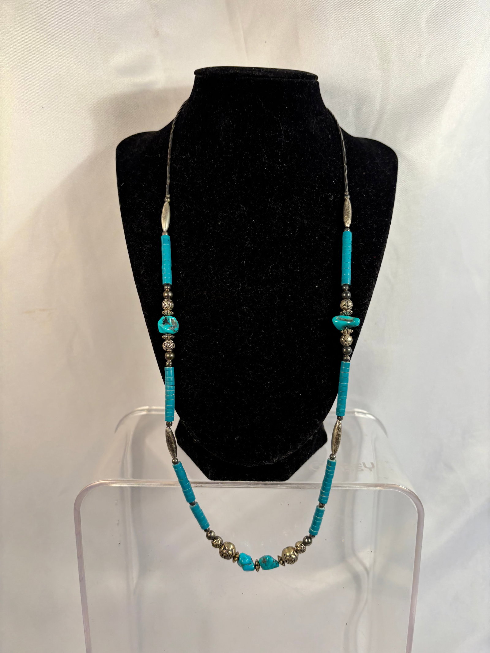 Turquoise and Silver-Tone Heishi Bead Necklace: A Southwestern-style necklace featuring turquoise heishi beads and irregular turquoise stone beads, interspersed with decorative floral-form beads, spherical spacers, and elongated silver-tone beads. 