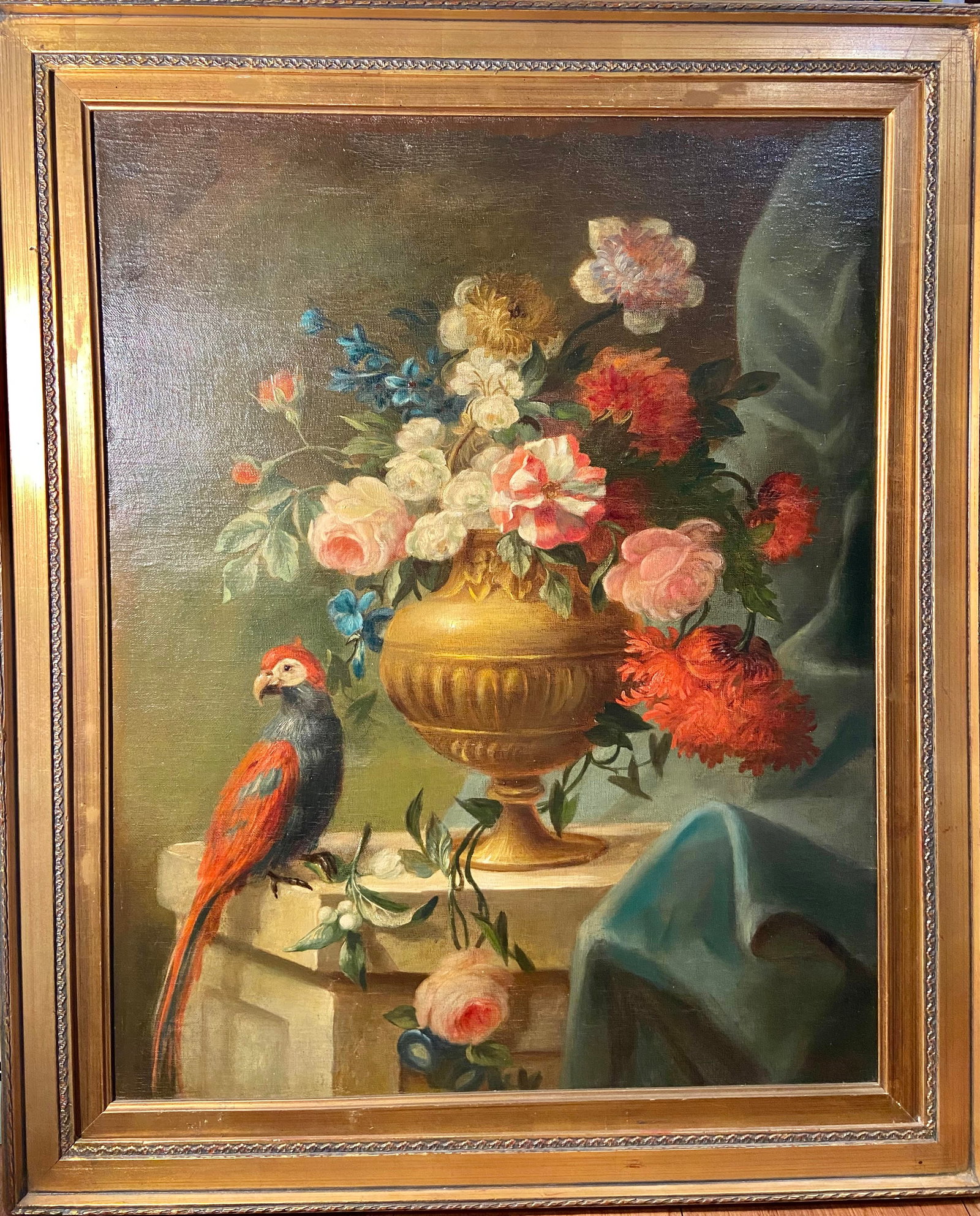 European style Oil on Canvas, Parrot and Floral Urn Still Life: Oil on canvas depicting a decorative still life scene featuring a vividly colored parrot perched on a stone ledge beside a classical gilt urn filled with lush floral arrangements. The bouquet includes