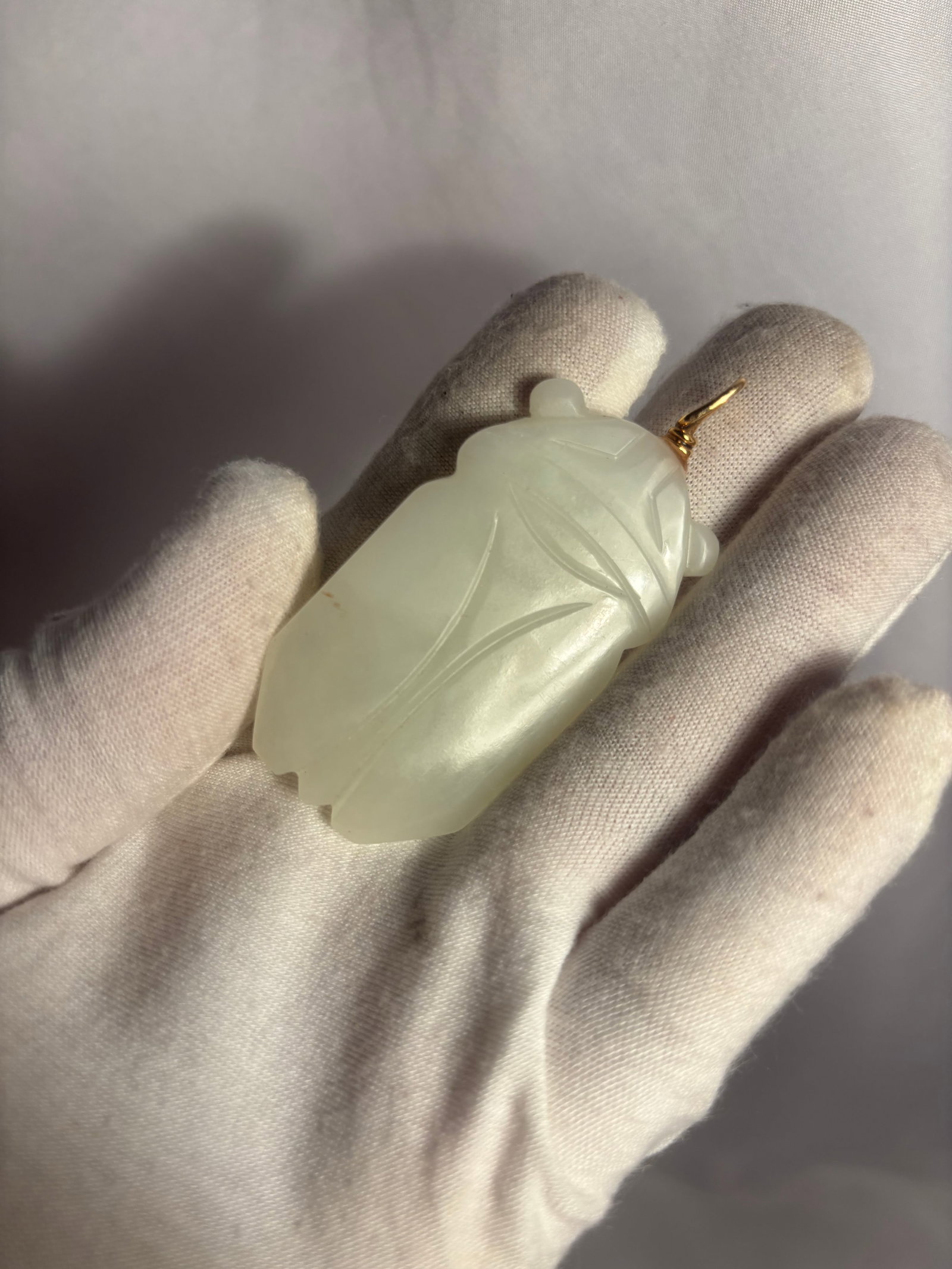 Chinese Pale Celadon Jade Cicada Pendant: A Chinese pale celadon jade pendant finely carved in the form of a cicada, with stylized wings and delicately incised details defining the body and wing structure. The stone displays a soft pale celad