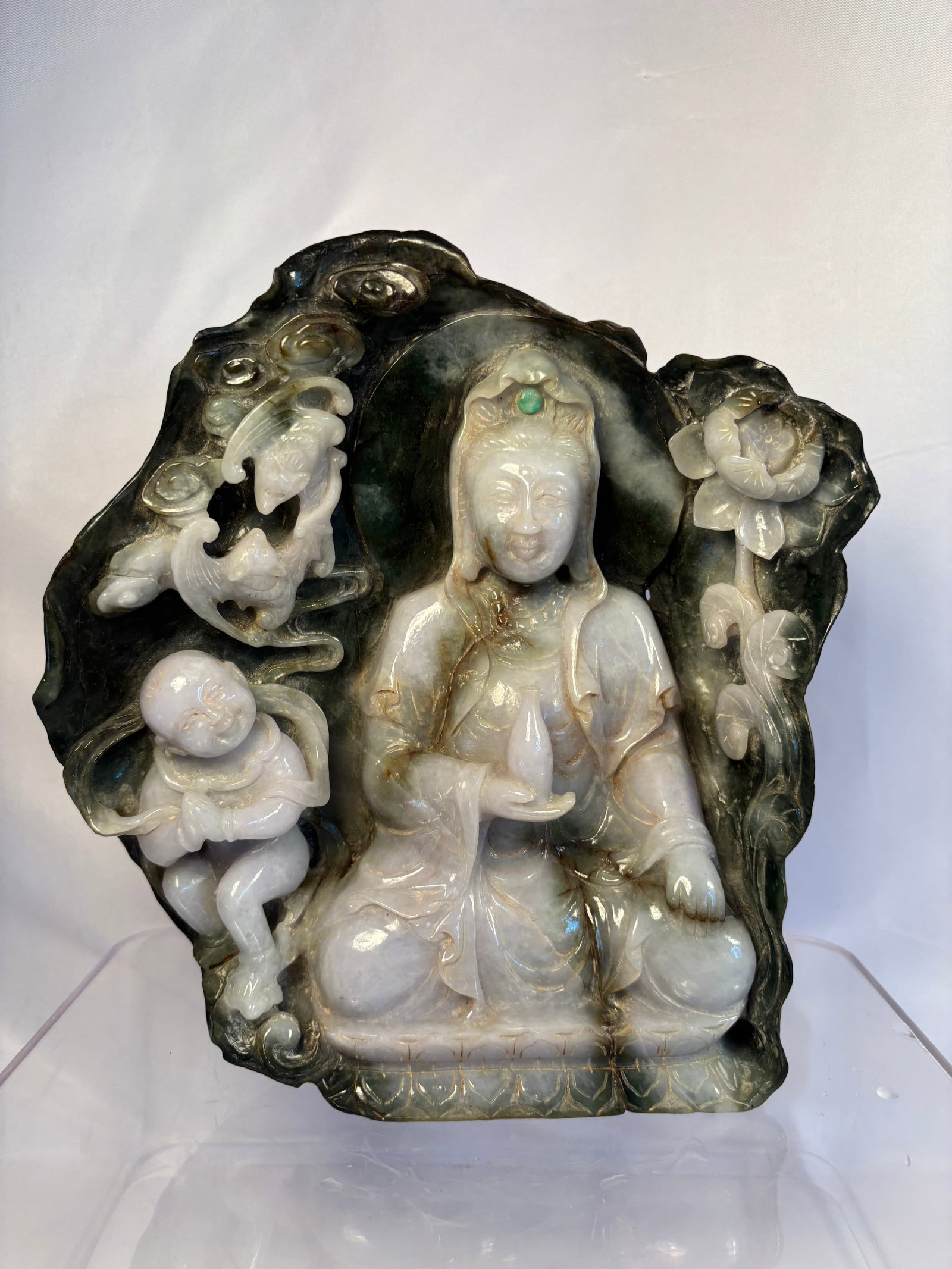 Chinese Two-Tone Jadeite Boulder Carving of Guanyin, Child and Phoenix: A Chinese sculpture carved from a single substantial two-tone jadeite boulder, depicting Guanyin holding a vase and accompanied by a child attendant, phoenix, and flowering peonies. The pale gray-gree