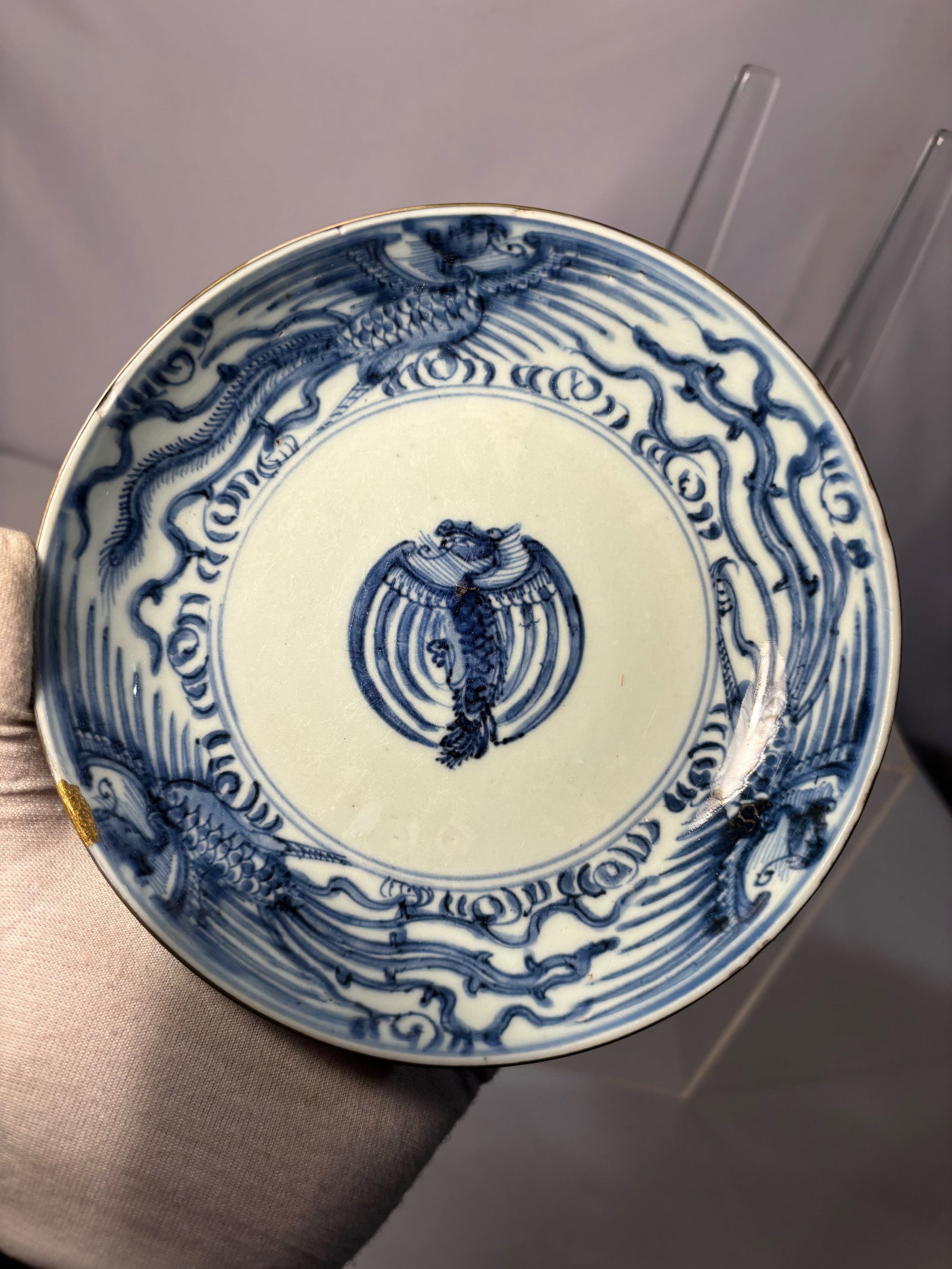 A Chinese Blue and White Double Dragon Plate, Transitional Style, Late Ming to Early Qing: A Chinese blue and white porcelain plate decorated in underglaze cobalt with two animated dragons encircling a central phoenix medallion. The dragons are depicted in lively movement amid scrolling clo
