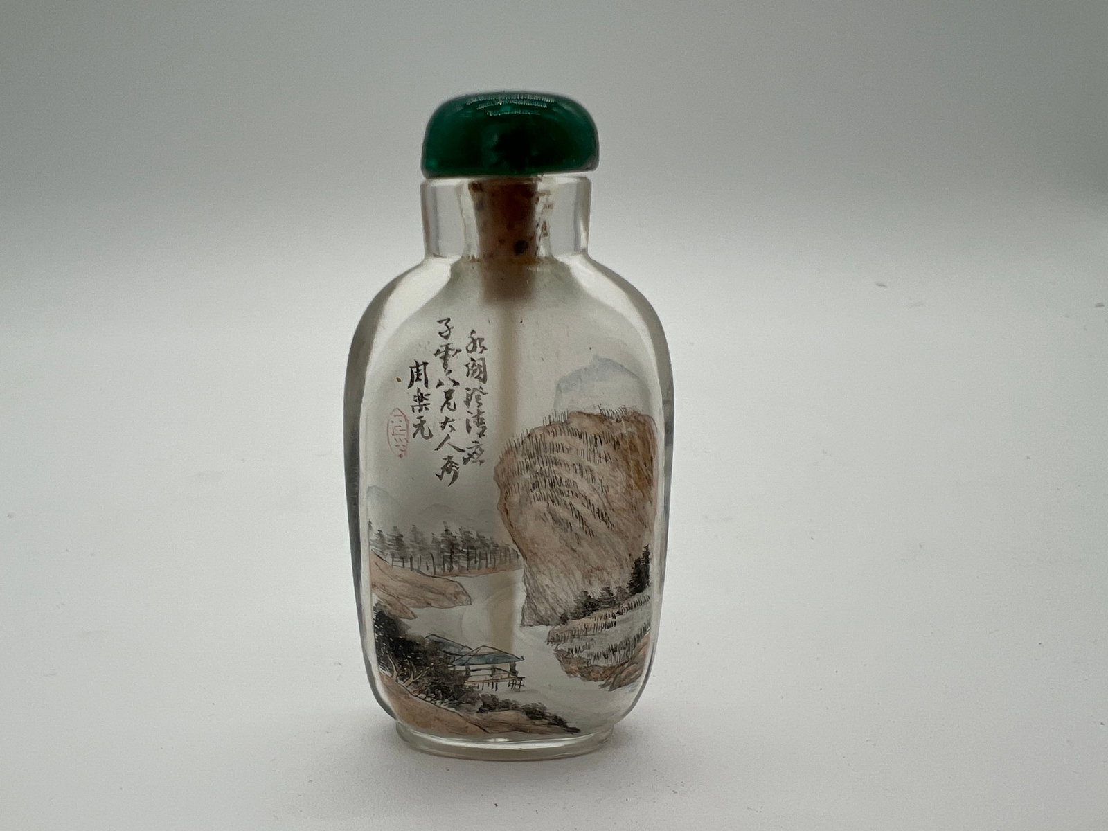 An Reverse painted glass snuff bottle signed Zhou Leyuan: Late 19th century; The landscape painting inside your bottle depicts natural scenery, including mountains, trees, and a figure, while the reverse side has a poetic inscription in Chinese. glass