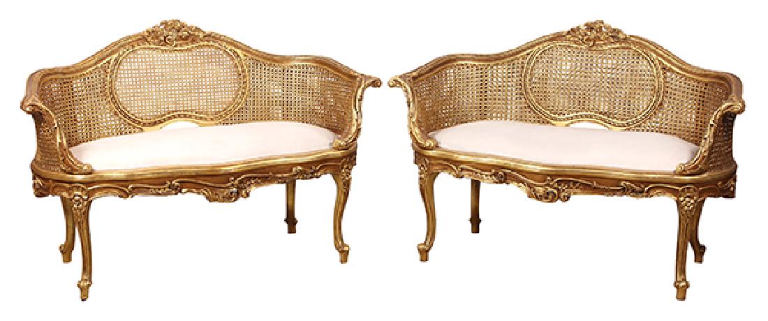 Pair of Louis XV style giltwood settees: Pair of Louis XV style giltwood settees, each having a floral decorated crest, above the cane back, continuing to a cream upholstered seat, and rising on cabriole legs, 34"h x 50"w x 22"d