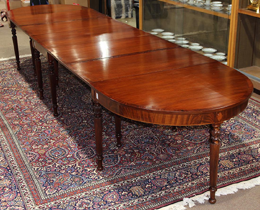 Regency style mahogany dining table: Regency style mahogany dining table, in three parts, each having band inlay, the two corner pieces with a single drop leaf, the central part with two drop leaves, and rising on reeded and tapered legs