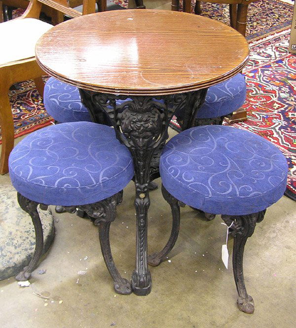English Oak, Iron Pub Table, Stools: English oak and iron pub table with four stools, the round oak top over cast figural iron base together with four matching stools each with blue upholstered padded seat over cast iron base with splaye