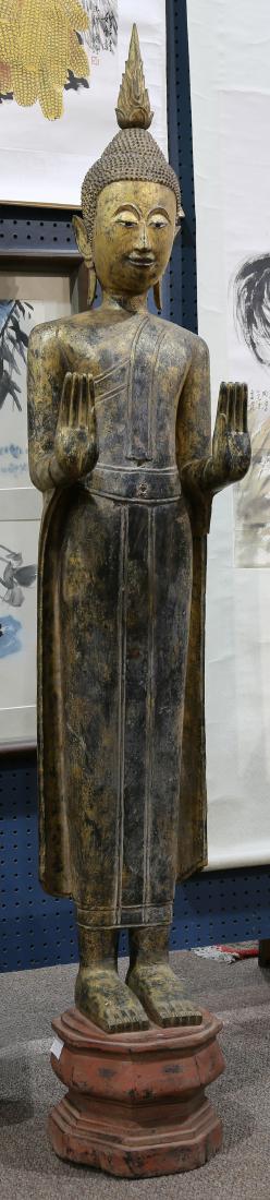 Thai Large Gilt Wood Buddha: Thai large gilt wood Buddha, in monastic robe and hands in abhaya mudra, standing above a red pedestal, 67"h