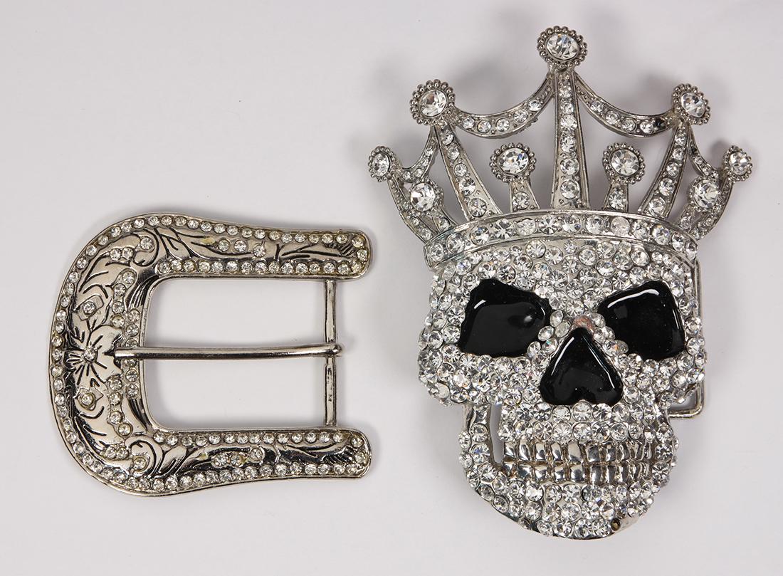 Metal belt buckles: (Lot of 2) Metal belt buckles including 1) crowned skull, white stone and white metal belt buckle, measuring approximately 5.5 X 4.5 inches (several stones missing); together with 1) white stone and w