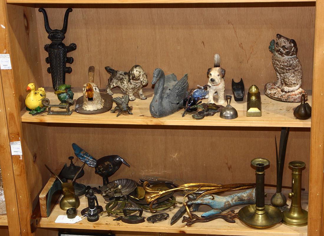Two shelves of vintage cast iron, brass and other: Two shelves of vintage cast iron, brass and other metalware items including animal figures, doorstops, a bootjack, a nutcracker, pushup candlesticks, trivets, a whistle hand form handle, and flower or