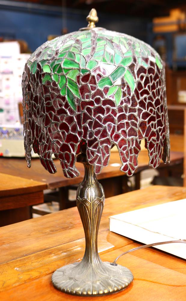 Tiffany style leaded glass table lamp: Tiffany style leaded glass table lamp, having a multi colored shade in greens to reds, and rising on a patinated base, 21"h x 11"w
