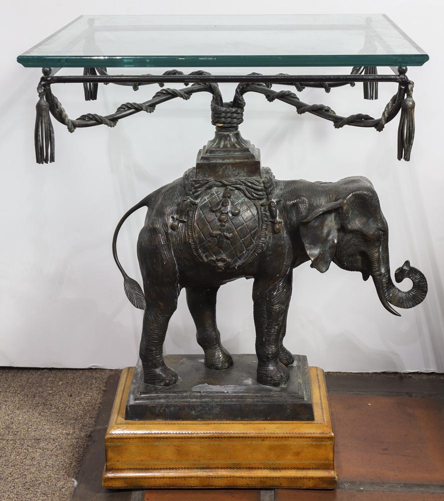 A Maitland-Smith bronze elephant occasional table: A Maitland-Smith bronze elephant occasional table, having a plate glass top, above a figural support of an elephant and rising on a conforming wood base, 26"h x 19.5"w x 19"d