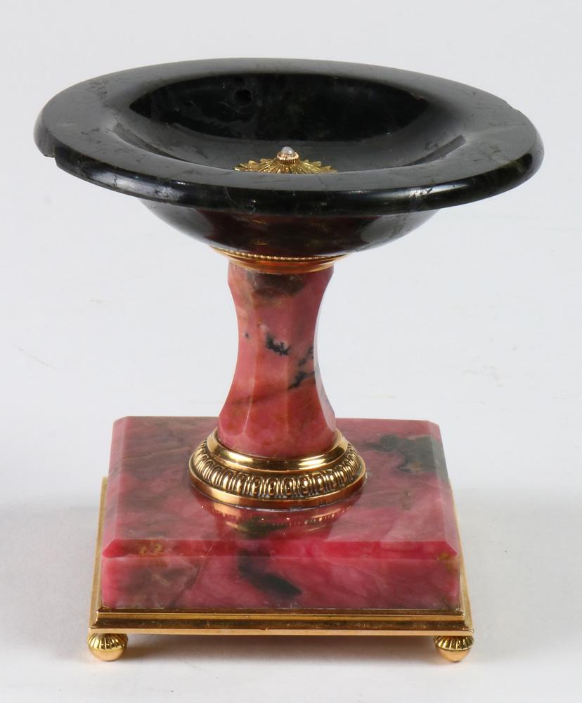 A Russian 14k mounted rhodonite and laboradite: A Russian 14k mounted rhodonite and laboradite miniature tazza for rings, bearing August Hollming for Faberge marks, the polished black stone shallow bowl centering a gold rosette, rising on a lavende