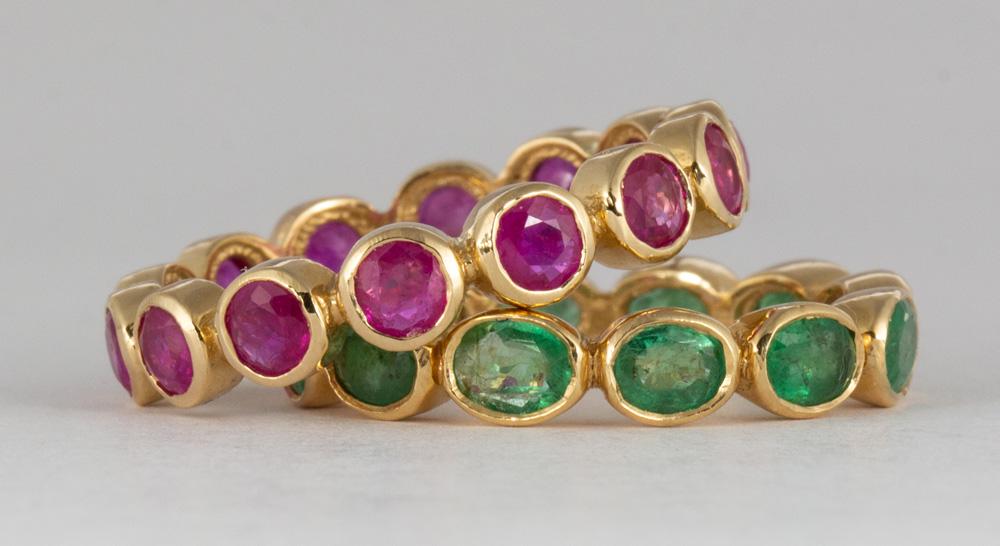 (Lot of 2) Emerald, ruby, 18k yellow gold eternity: (Lot of 2) Emerald, ruby, 18k yellow gold eternity bands Including 1) eternity band, featuring (12) oval-cut emeralds, weighing a total of approximately 2.15 cts., set in 18k yellow gold, size 5.5; to