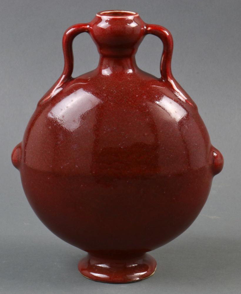 Chinese Copper Red Glazed Porcelain Moon-flask Vase: A Chinese copper red glazed porcelain moon-flask vase, of flattened circular shape raised on a low foot rim rising to a garlic bulb neck and set with two scroll handles, 8.5"w x 10"h