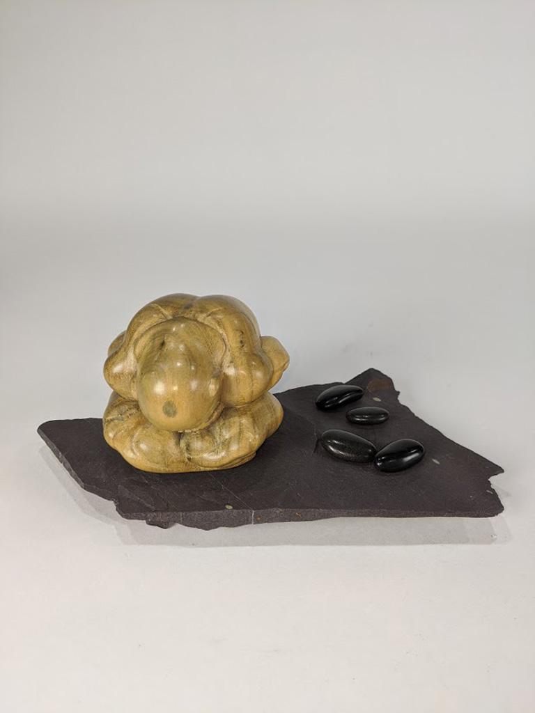 A Japanese Modern carved wood figure of a seated: Japanese Modern carved wood figure of a seated couching man, seated on a slate stand, with four additional stones, 4"h x 9"w Provenance: Property from the estate of late comedian / actor, Mr. Robin Wi
