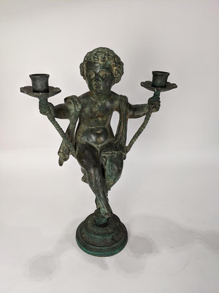 A Patinated metal candelabra in the Renaissance taste: A Patinated metal candelabra in the Renaissance taste, the two arm fixture centered by the seated putti, rising on a circular base, 21"h x 12.5"w